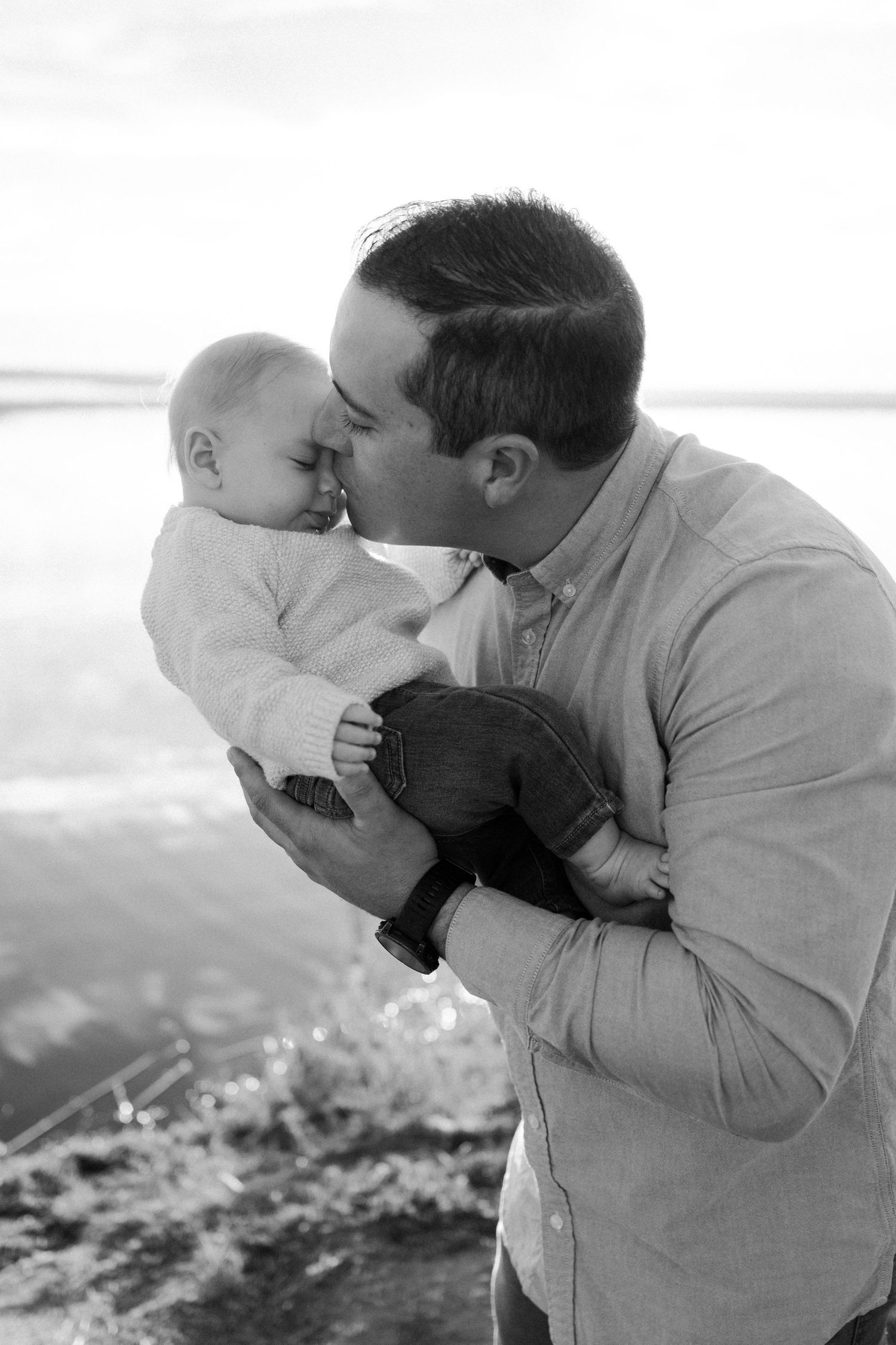 Black and white portrait of tender moment between parent and baby outdoors.