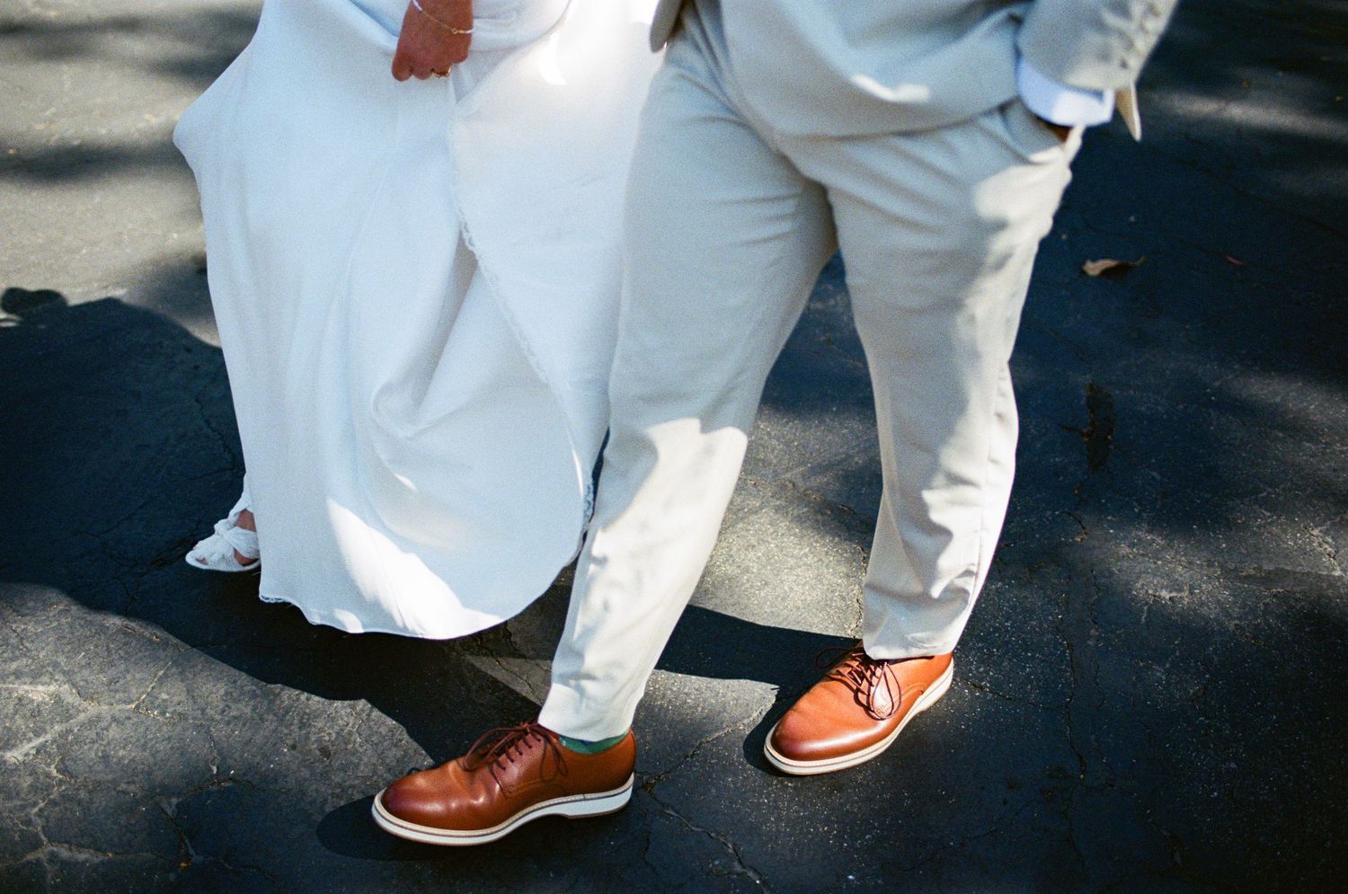 Close-up of bride and groom wearing matching brown leather oxford shoes at an outdoor wedding.