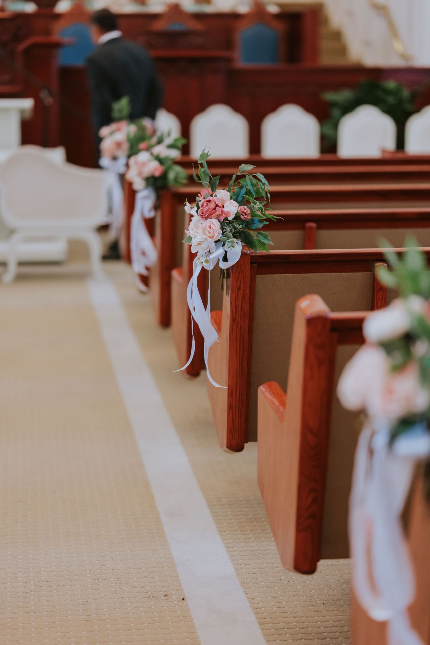 Church pews decorated with white bows and floral arrangements for a wedding ceremony.