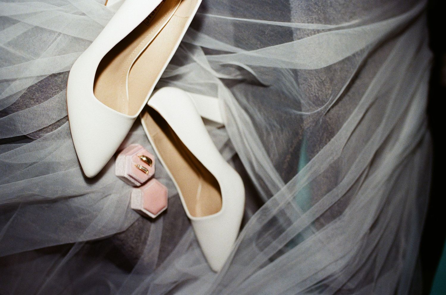 Elegant white wedding veil draped over beige high heel bridal shoes against a dark background.