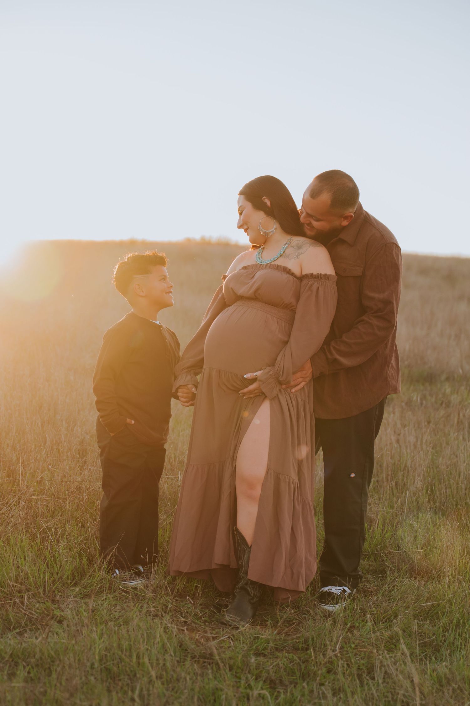 A group of people stand together in a grassy field at sunset with warm golden light illuminating the scene.