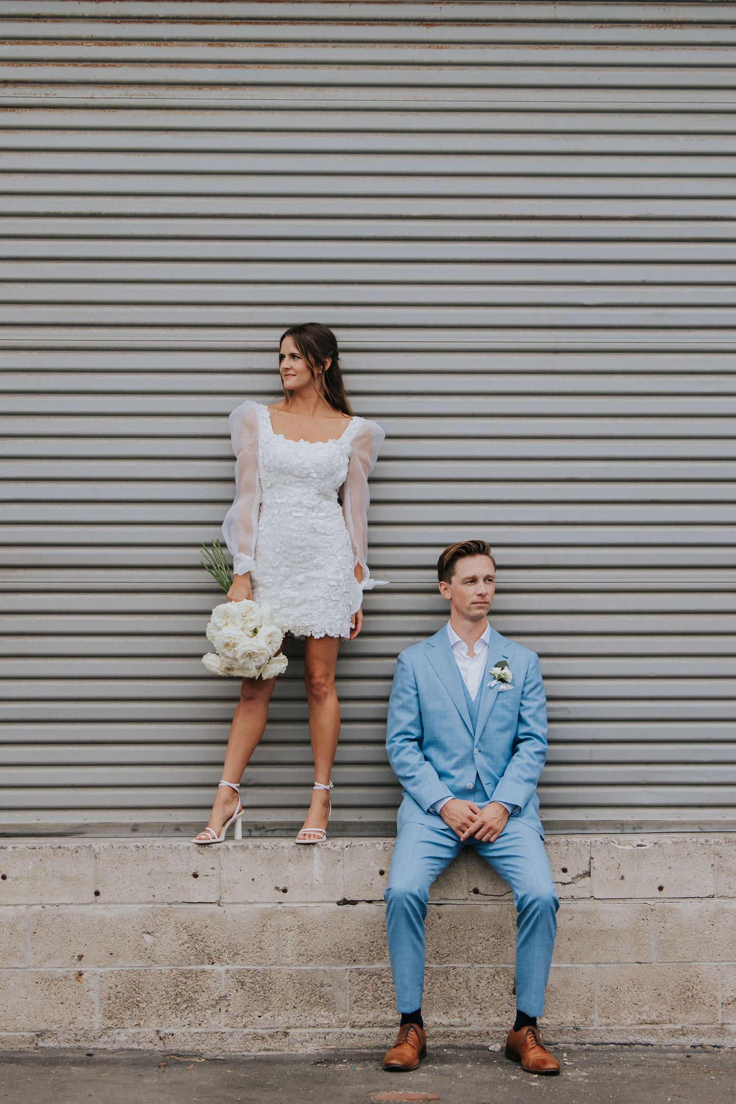 A stylish couple in wedding attire poses against a striped wall background for a modern photo shoot.