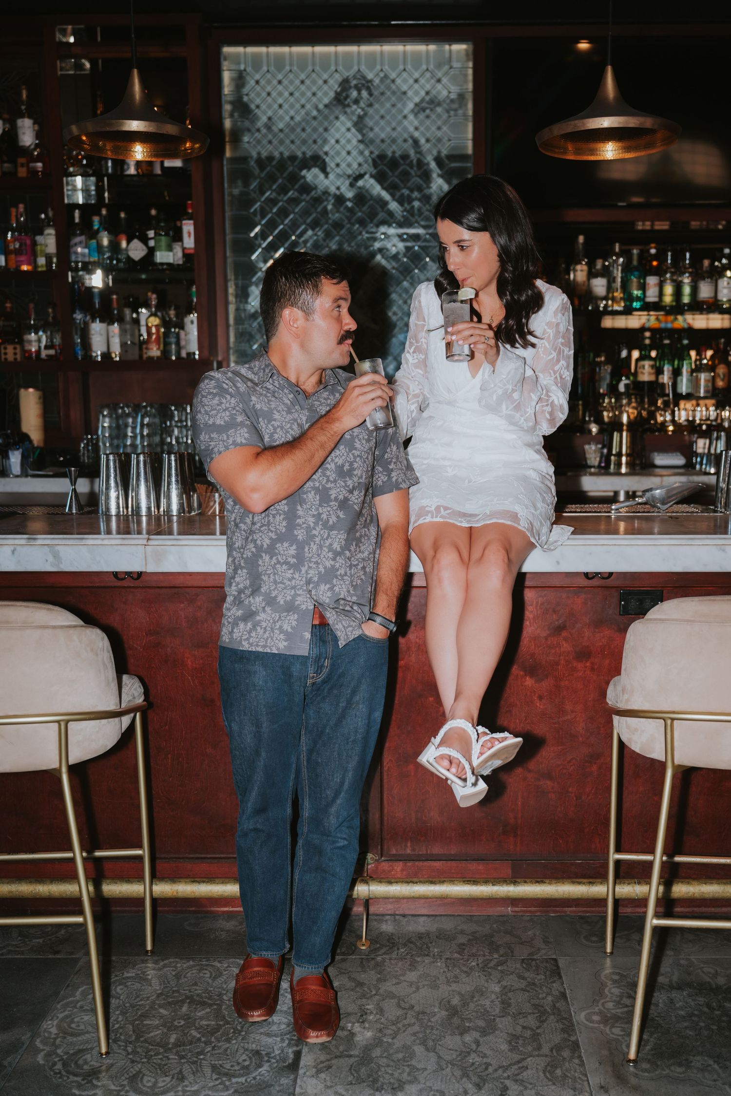 Couple in casual attire flirting and sharing playful moments at a bar with vintage-style lighting.