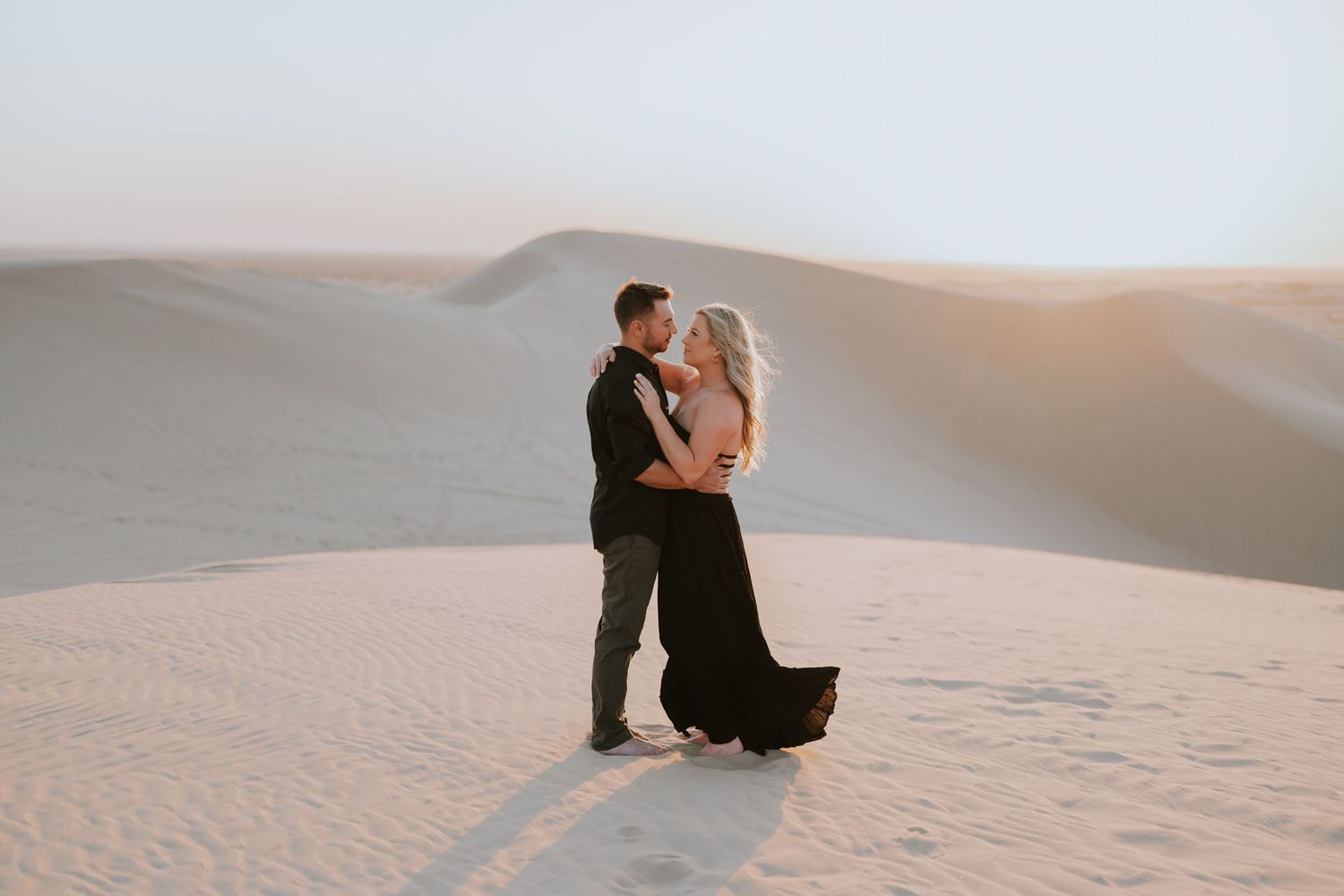 Couple sitting together on sand dunes during golden hour.