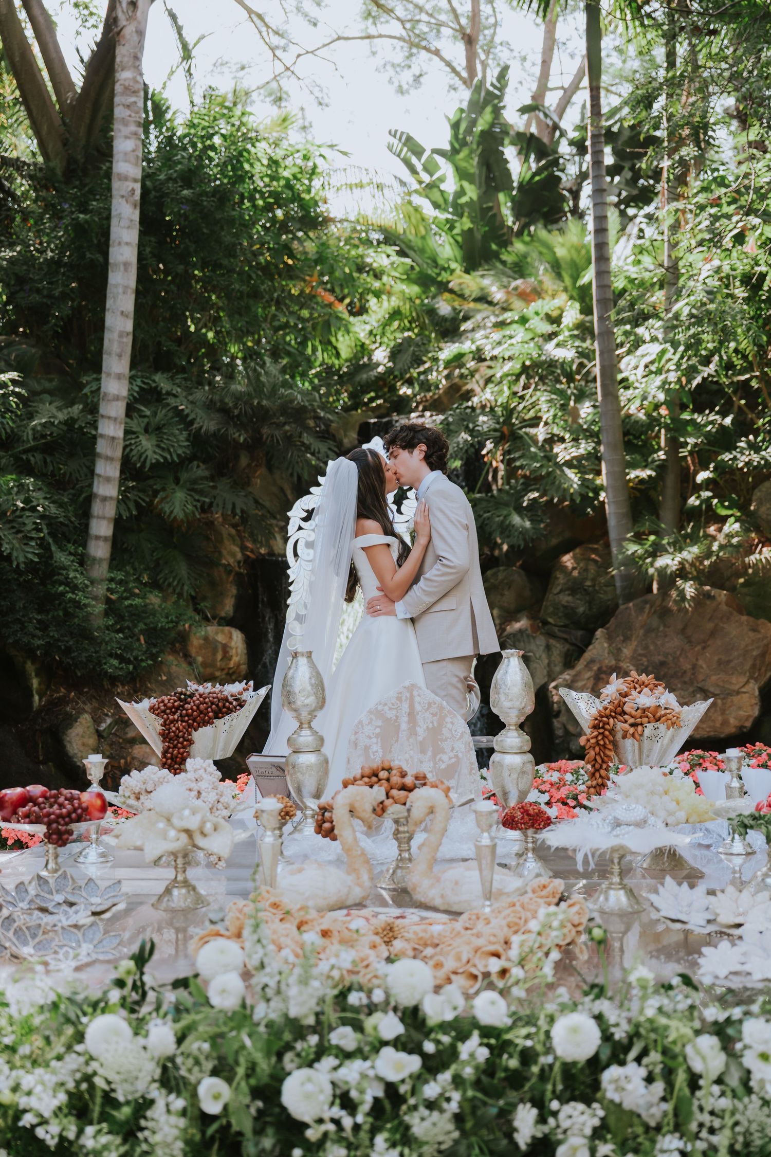 Elegant white wedding reception table decorated with flowers and candles in garden setting.