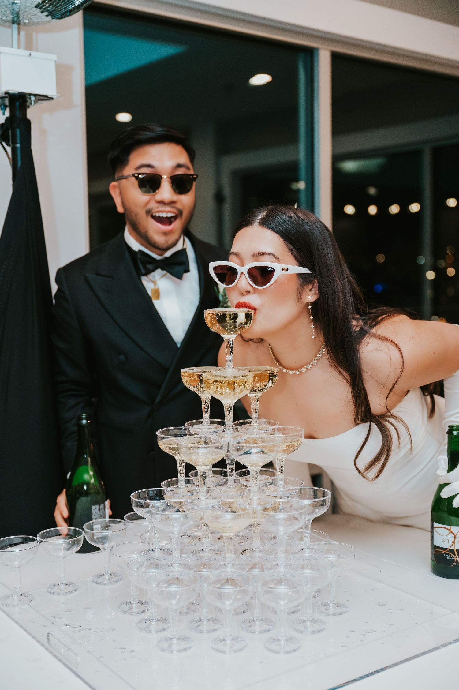 A wedding party pours champagne into a tower of stacked glasses at an elegant celebration.