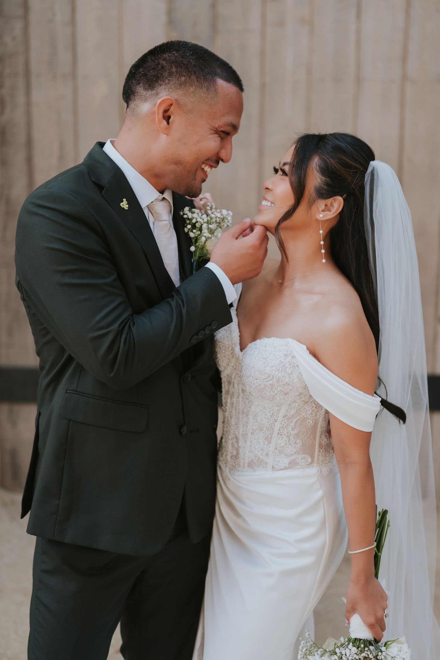 A romantic wedding portrait showing a couple in formal attire sharing an intimate moment against a neutral backdrop.