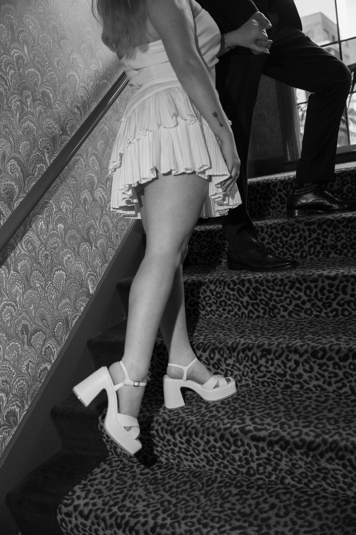 Bride in white mini dress and platform heels on leopard print stairs in black and white photo.