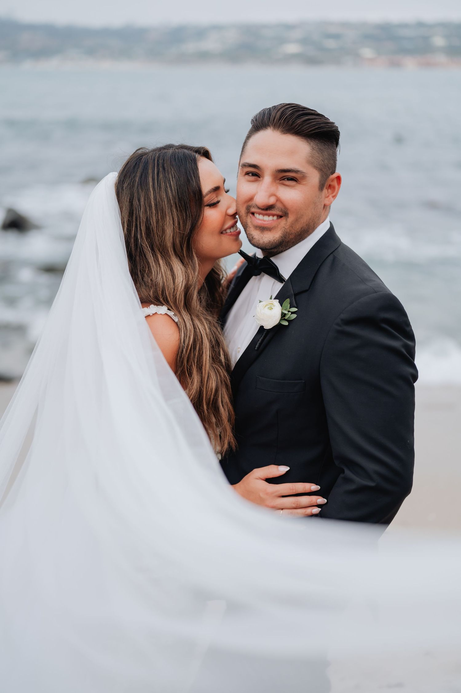 A romantic beachside wedding portrait with a flowing white veil catching the ocean breeze.