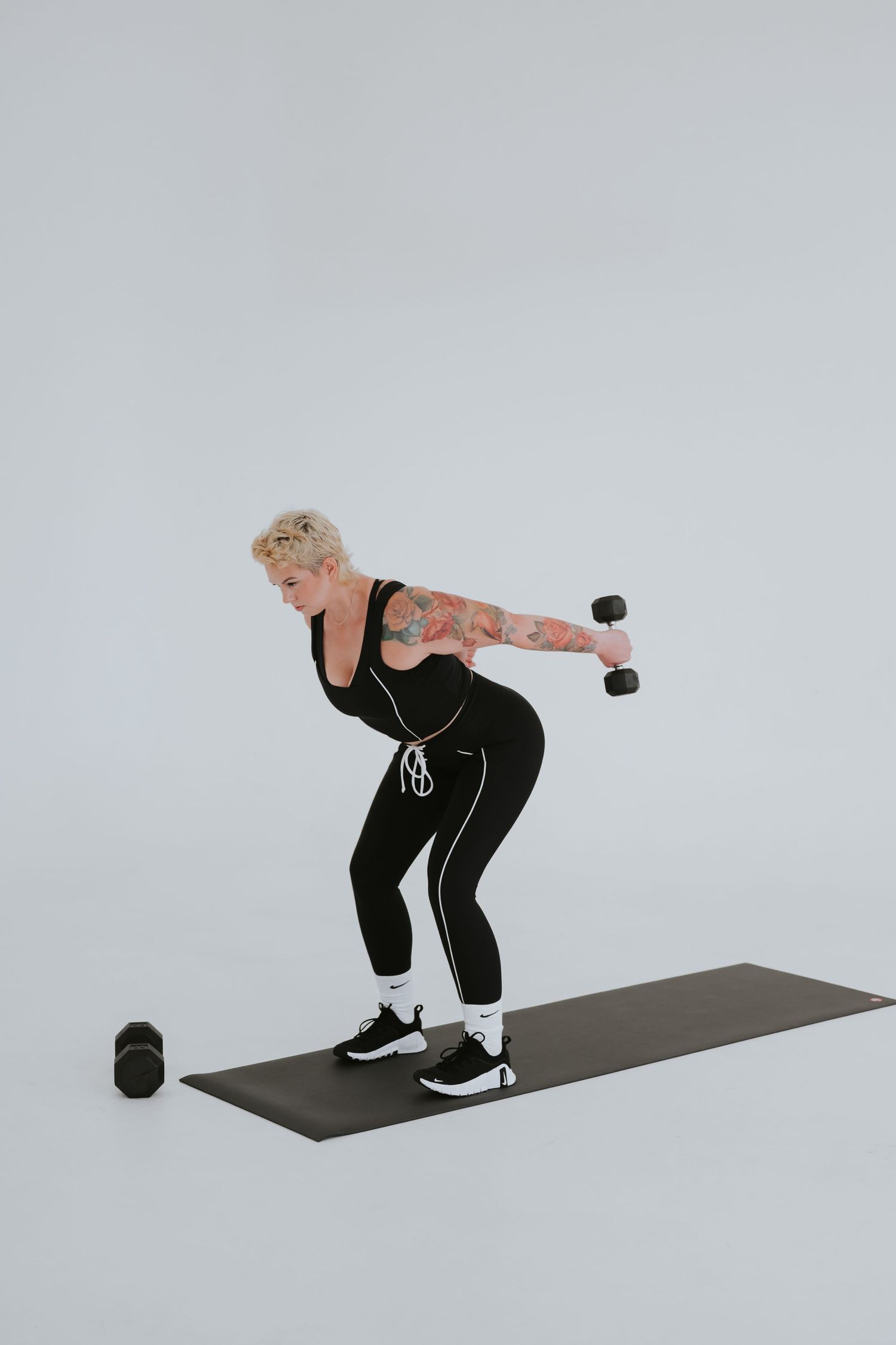 Person in black athletic wear performing a bent over row exercise with a dumbbell on a gray exercise mat.