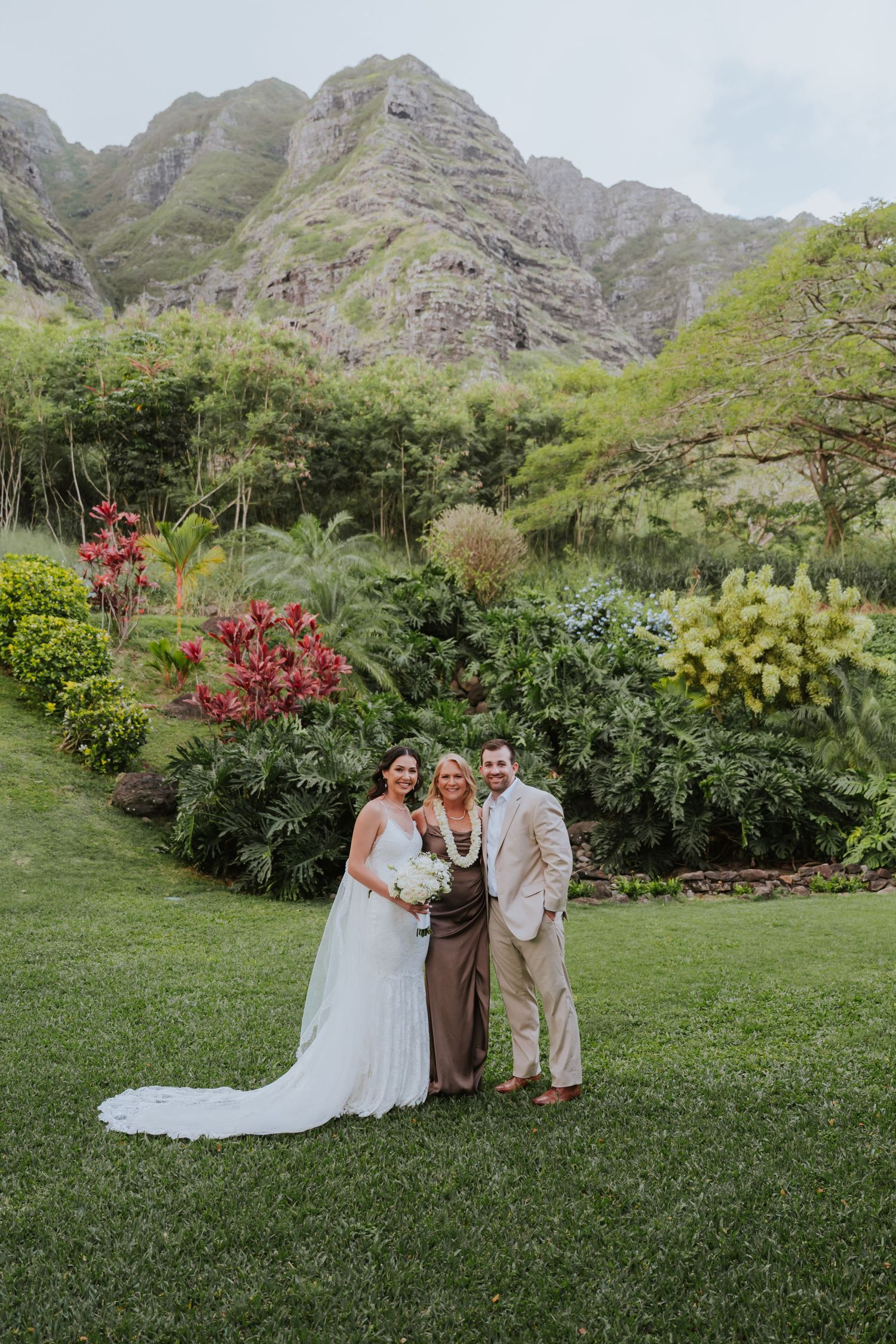 Outdoor wedding ceremony with dramatic mountain backdrop and tropical garden setting.