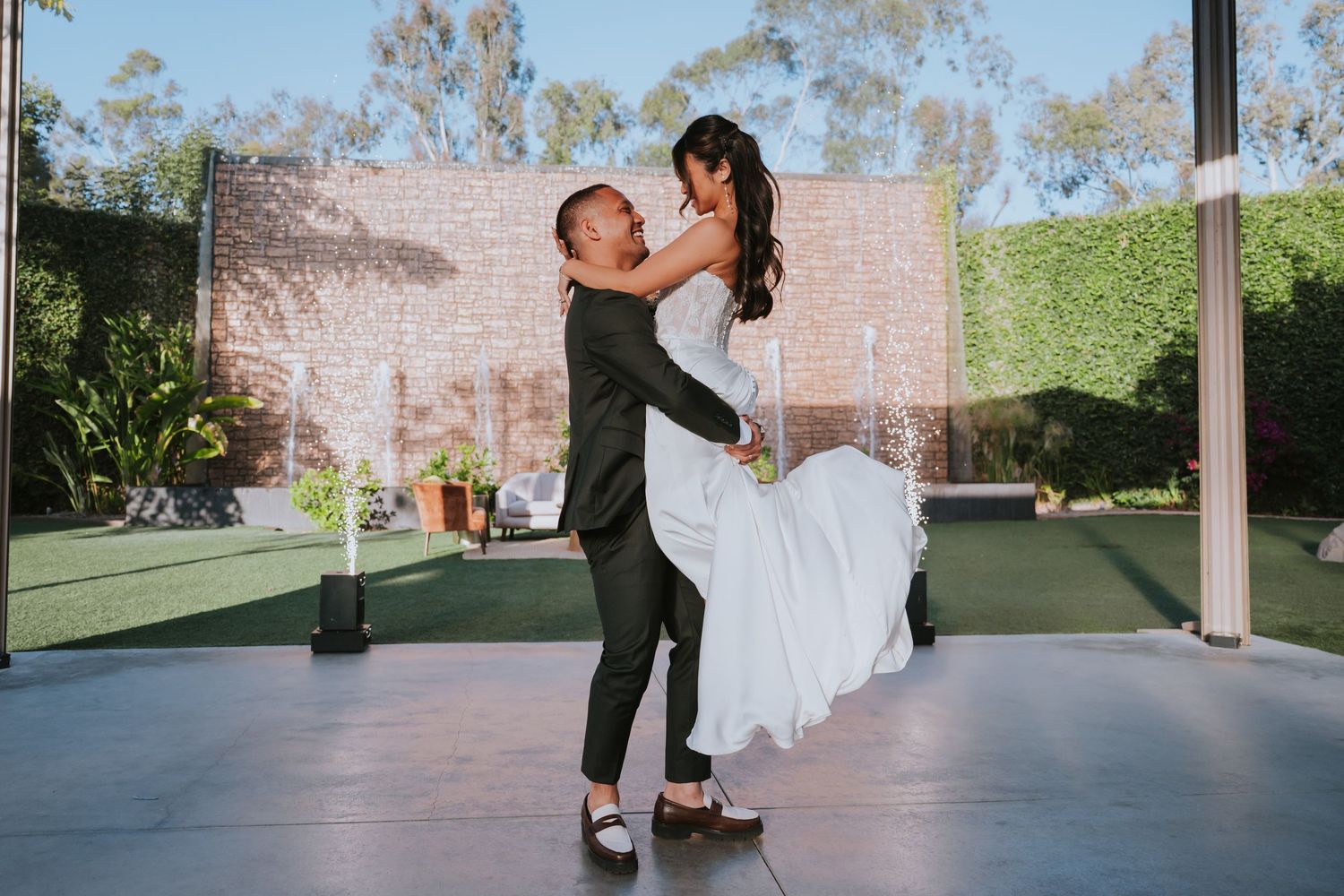 A couple in formal attire dances together on a covered outdoor patio with trees visible in the background.