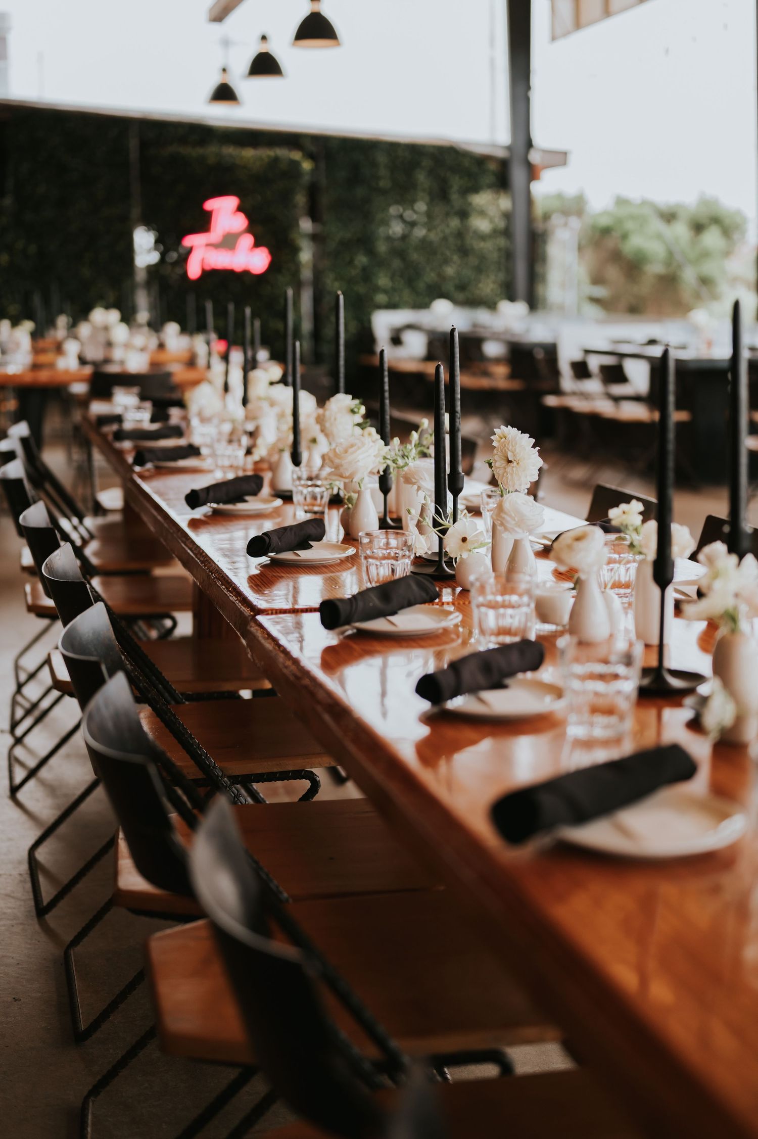 Long wooden banquet tables set for an elegant wedding reception with black chairs and white floral centerpieces.