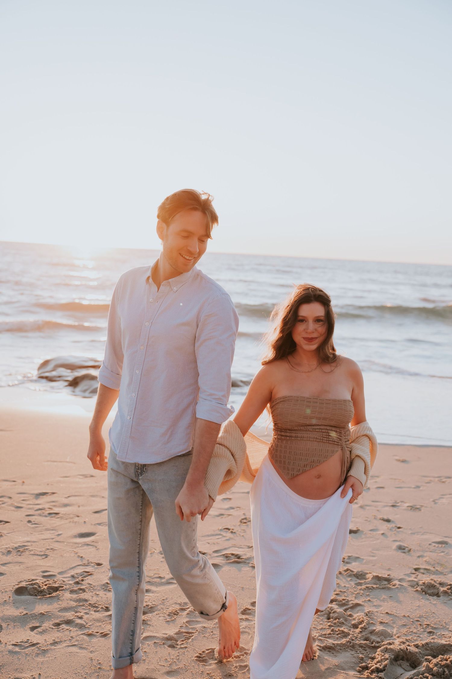 A couple walks together on a sandy beach at sunset in a romantic photo series.