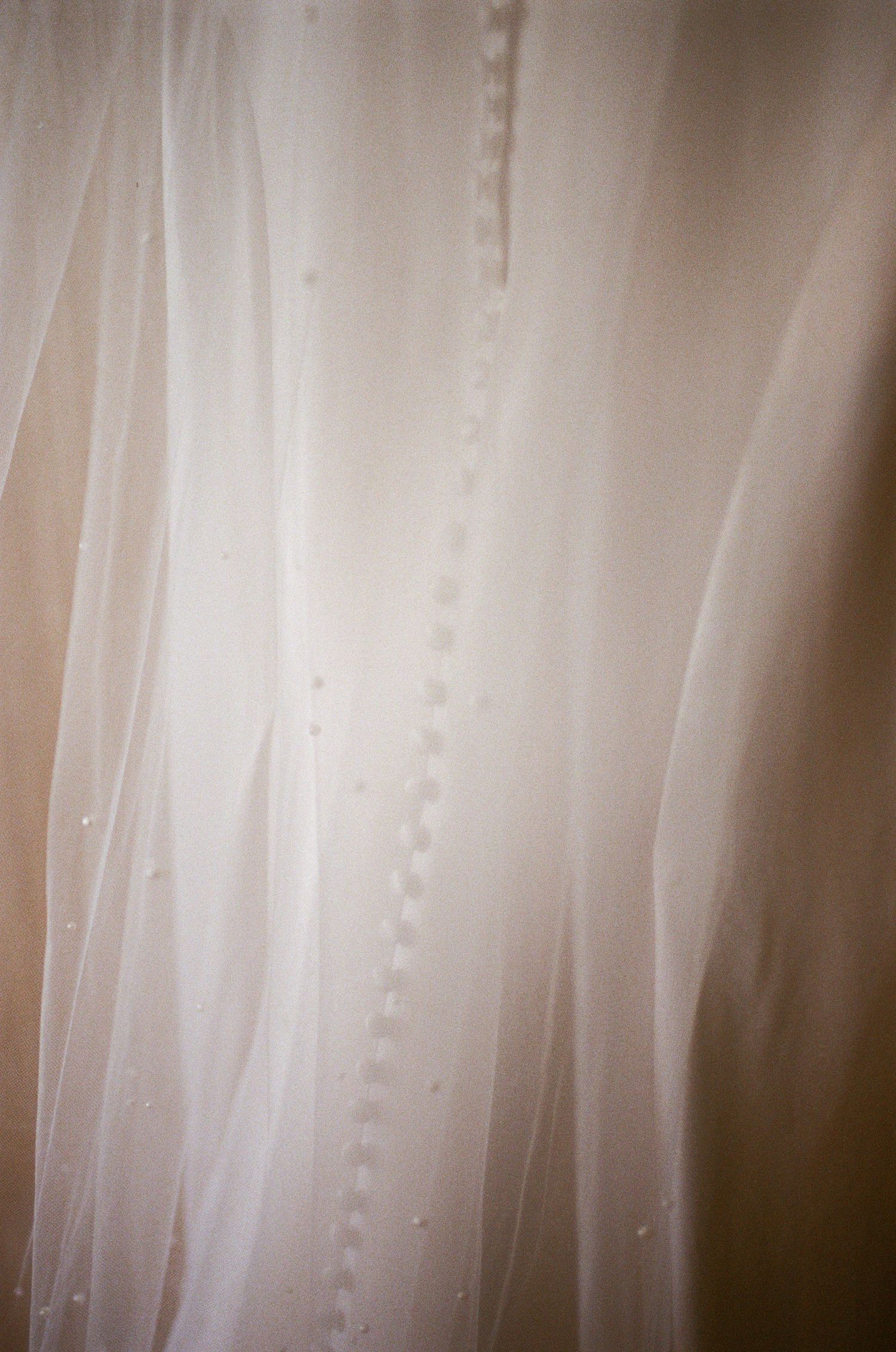 Close-up of a white wedding dress with delicate pearl button details and flowing sheer fabric.