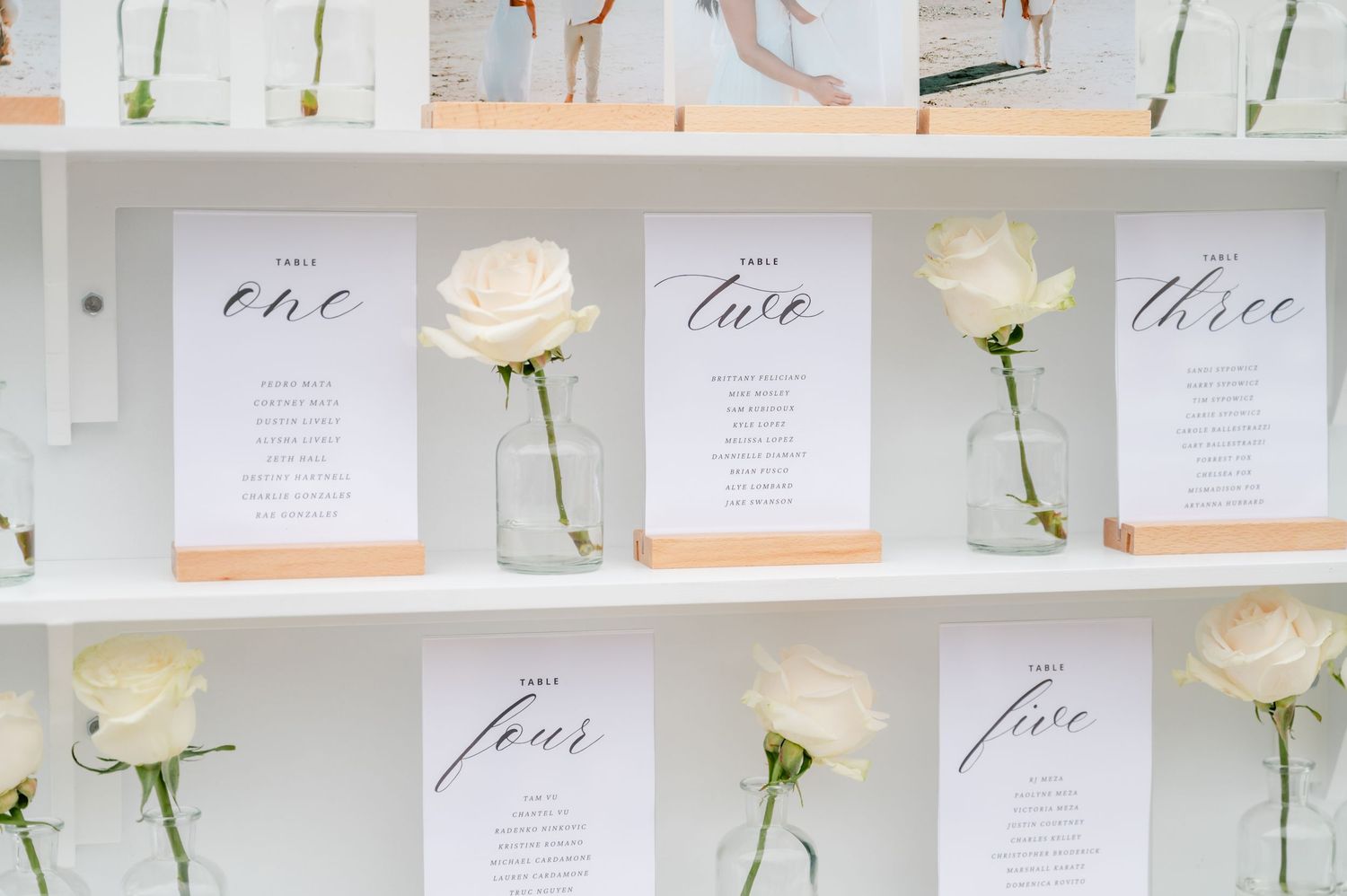 Close-up of white wedding seating chart display with individual roses in vases.