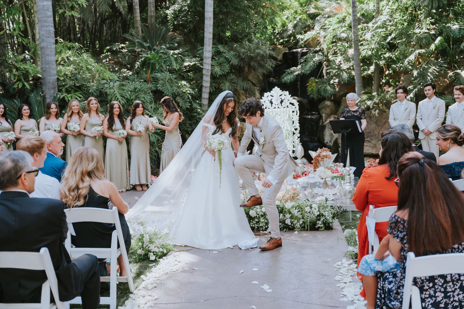 Garden wedding ceremony with guests seated and decorated aisle with white floral arrangements.