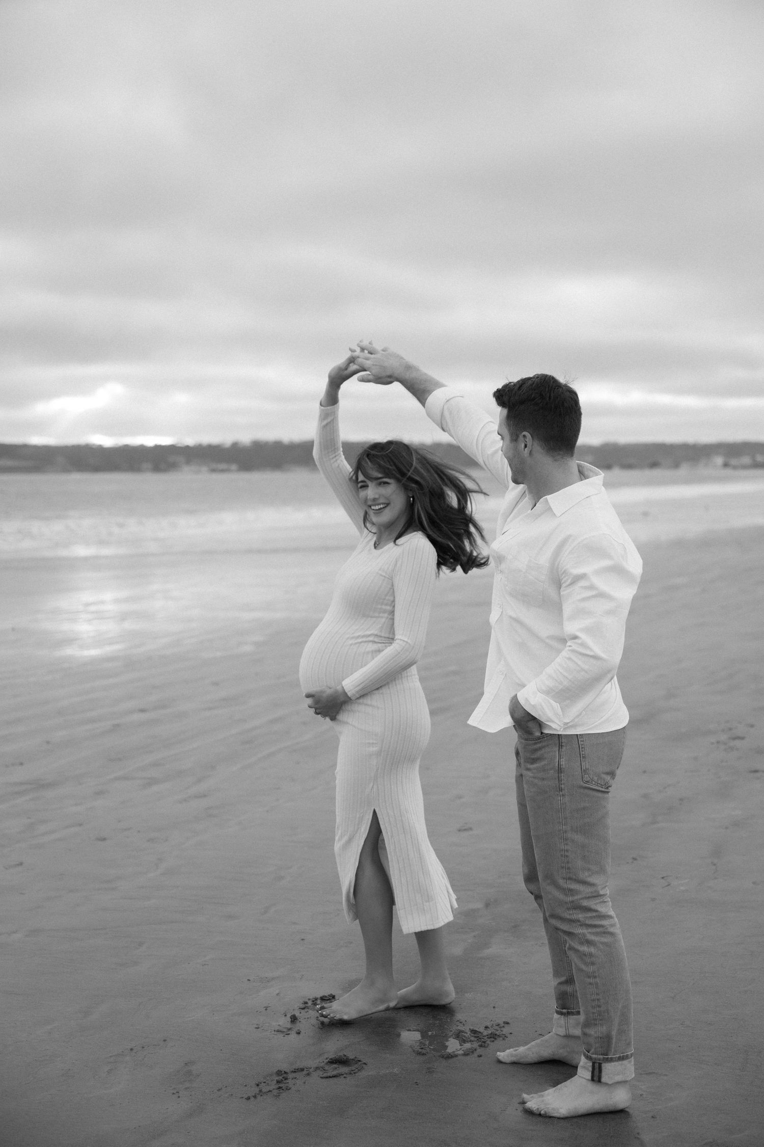 Couple dances playfully on a misty beach during sunset photo session.