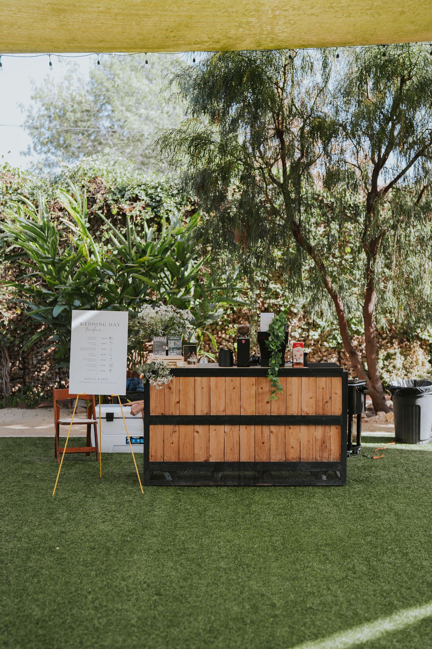 Modern wooden planter boxes with greenery line up on grass at an outdoor event space.