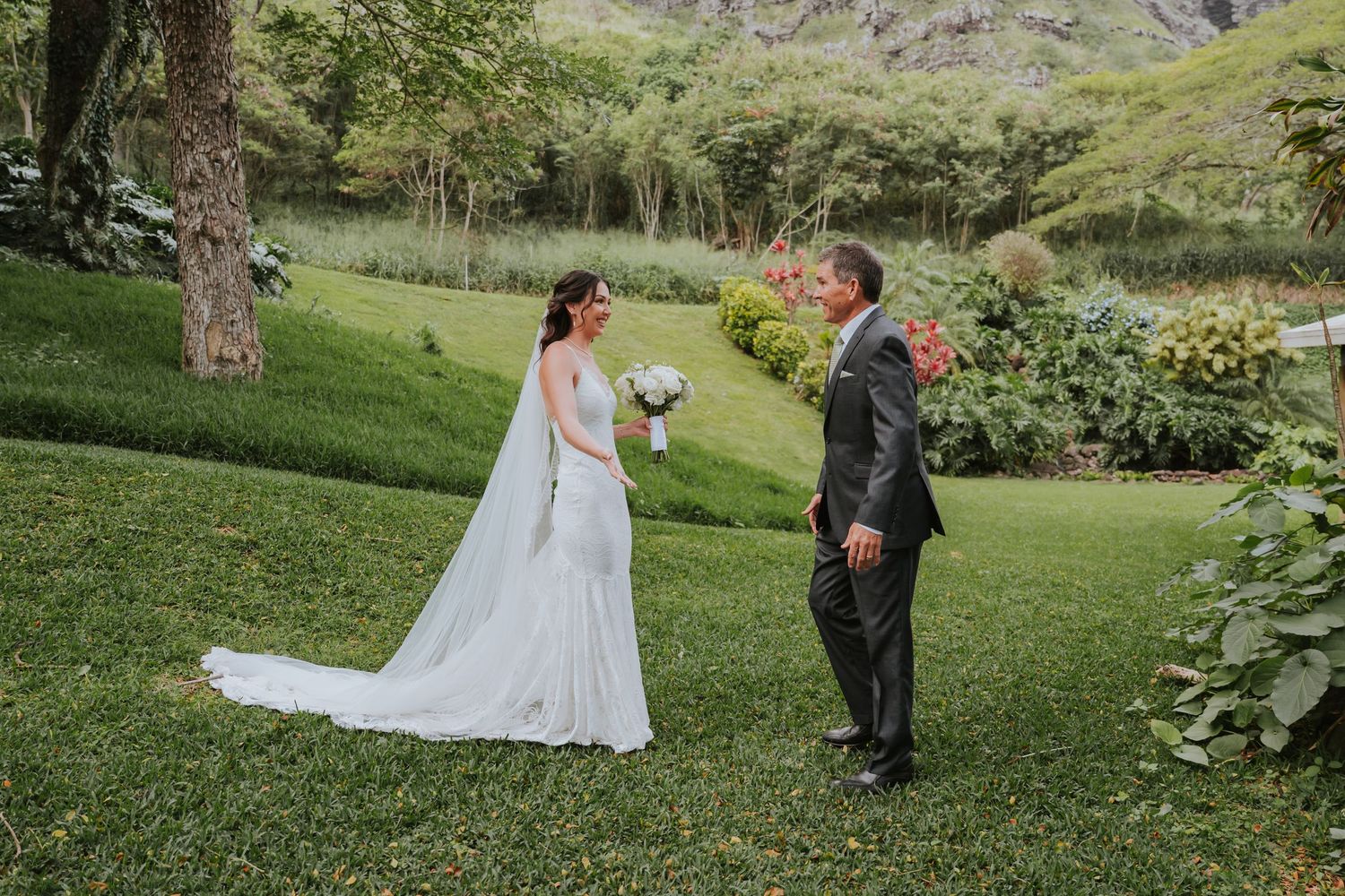 A romantic first look moment unfolds between a couple on a lush green hillside in Hawaii.