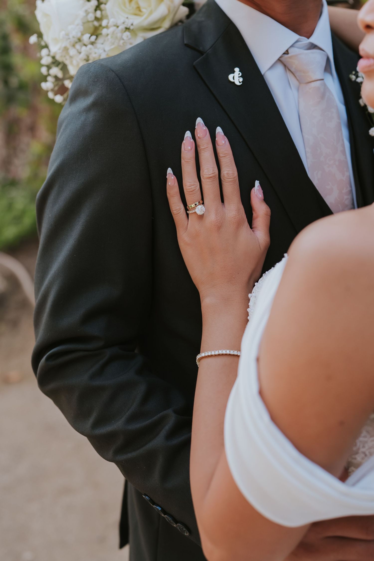 Close-up shot of a couple's formal attire showing a white dress and black suit with jewelry details.