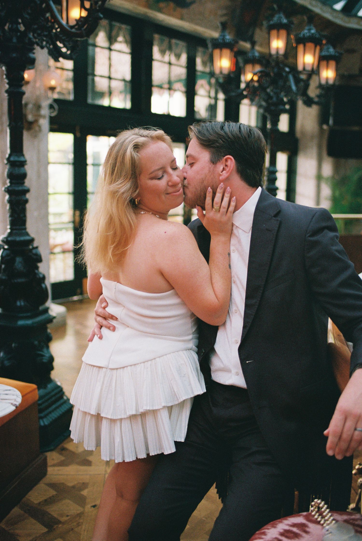 Couple sharing a romantic kiss in an upscale restaurant with ornate lanterns and dark wood decor.