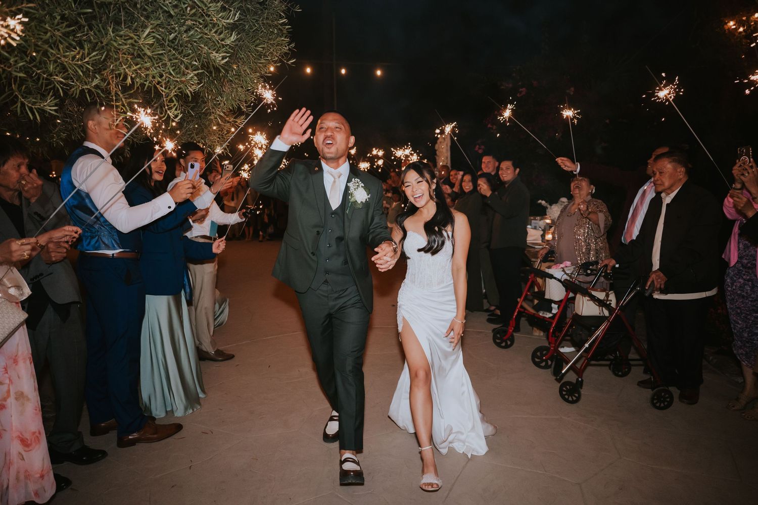 Wedding guests holding sparklers during nighttime celebration outdoors.