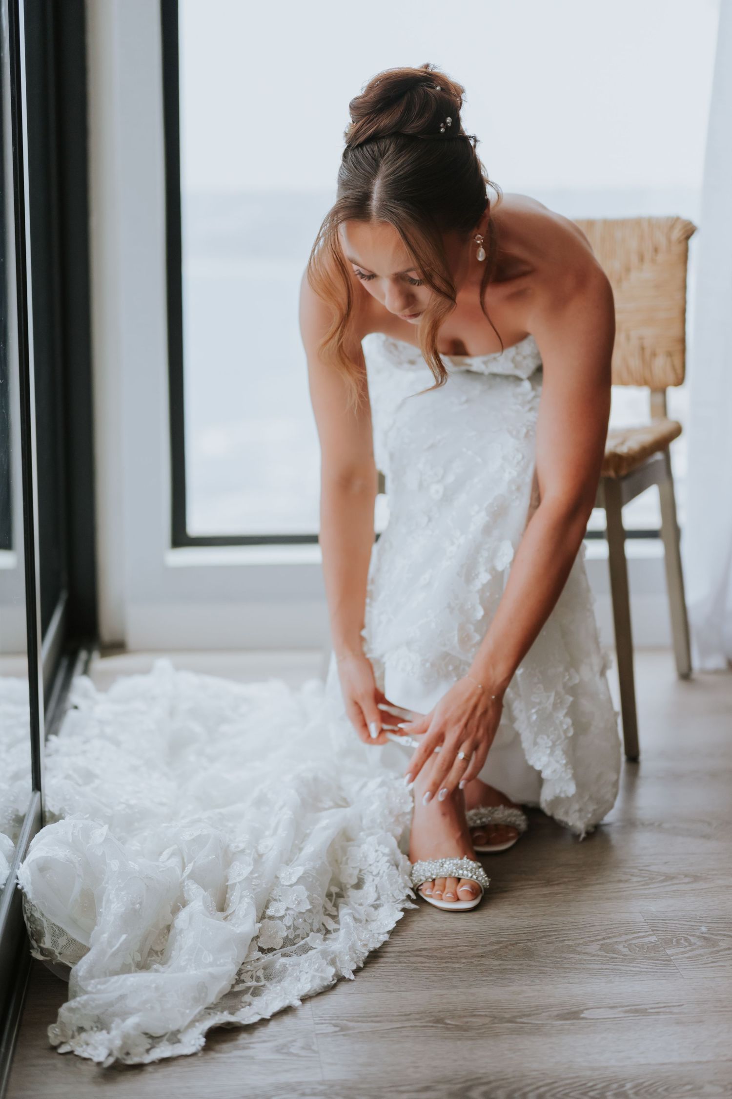 Close-up of a wedding dress as someone adjusts their shoes on a wooden floor.