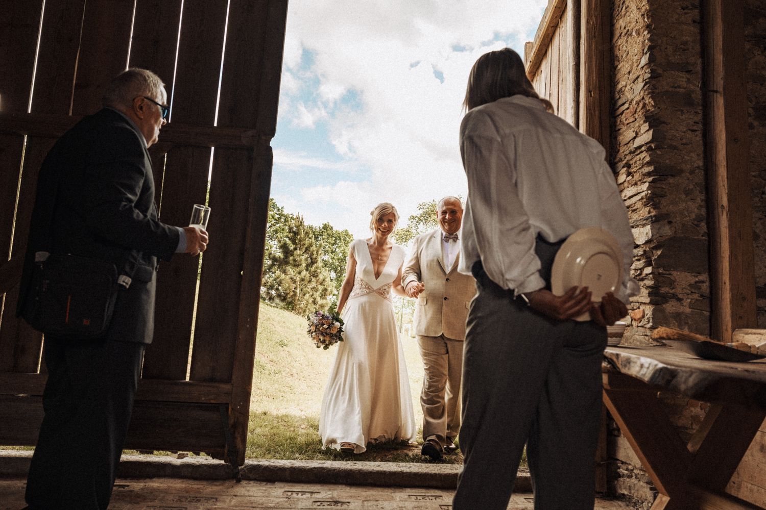 Looking through rustic doorway during intimate outdoor ceremony with couple and officiant visible in distance.