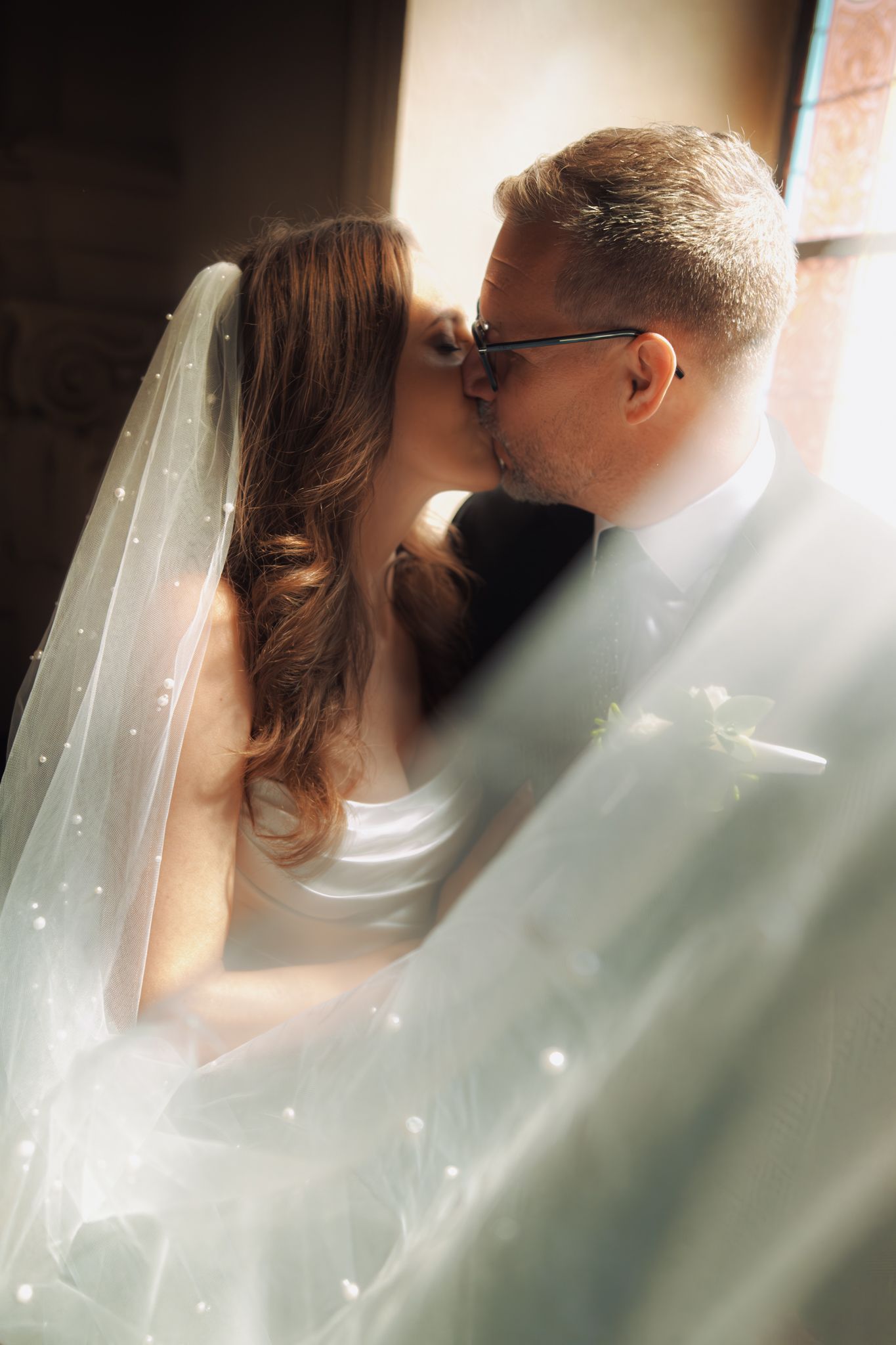 Romantický svatební portrét zachycující pár, který se intimně líbá za vlajícím bílým závojem.