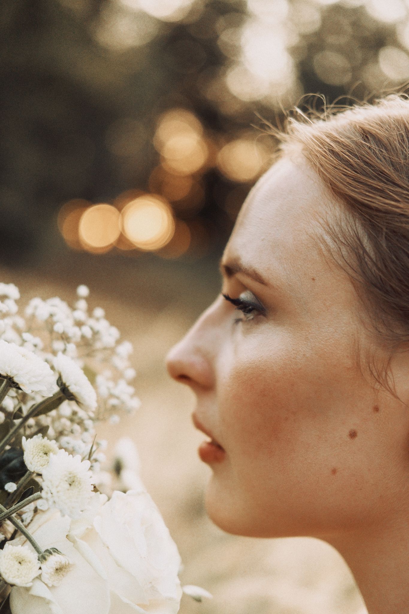 A close-up profile portrait with white flowers against a soft bokeh background in golden afternoon light.