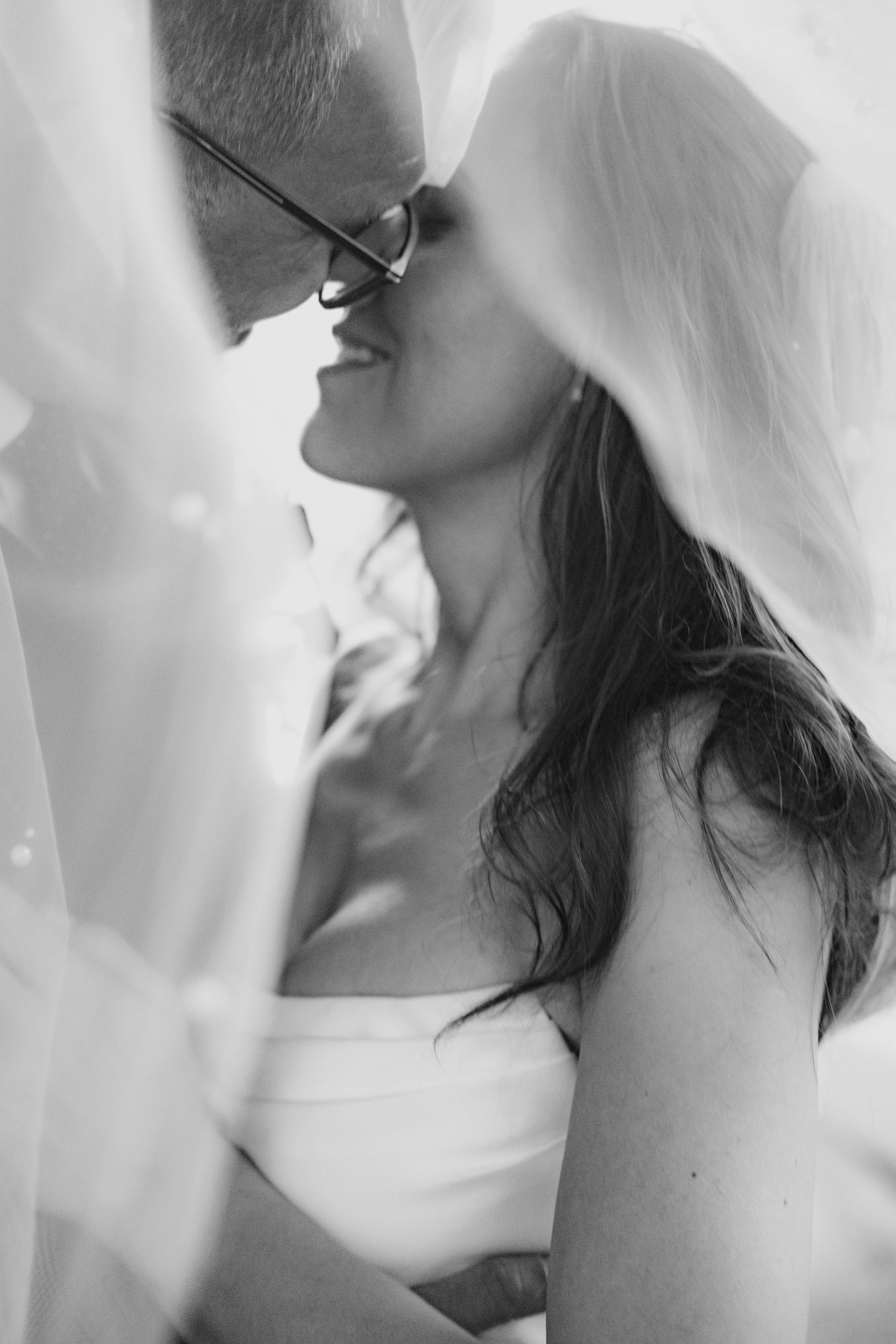 Black and white romantic wedding photograph showing couple sharing intimate kiss through bridal veil.