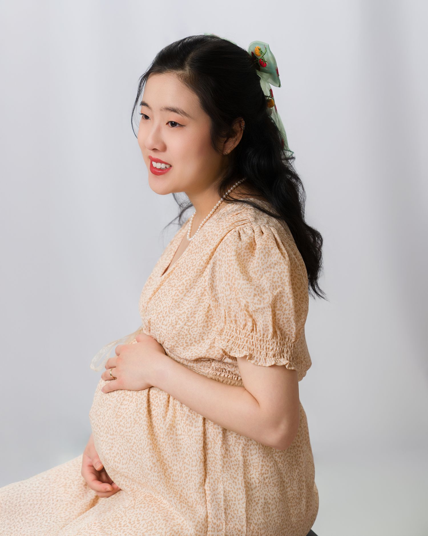 Maternity portrait of a pregnant woman in a floral summer dress, gently cradling her baby bump. Captured in a grace, side-profile