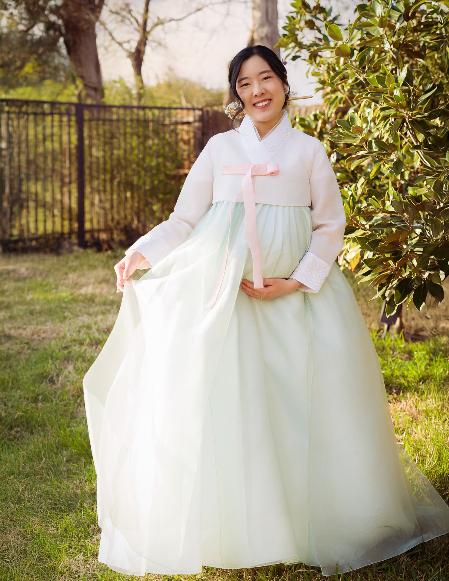 Maternity portrait of a pregnant woman in a HANBOK, Korean traditional, gently cradling her baby bump. Captured in a happy mo, smiling