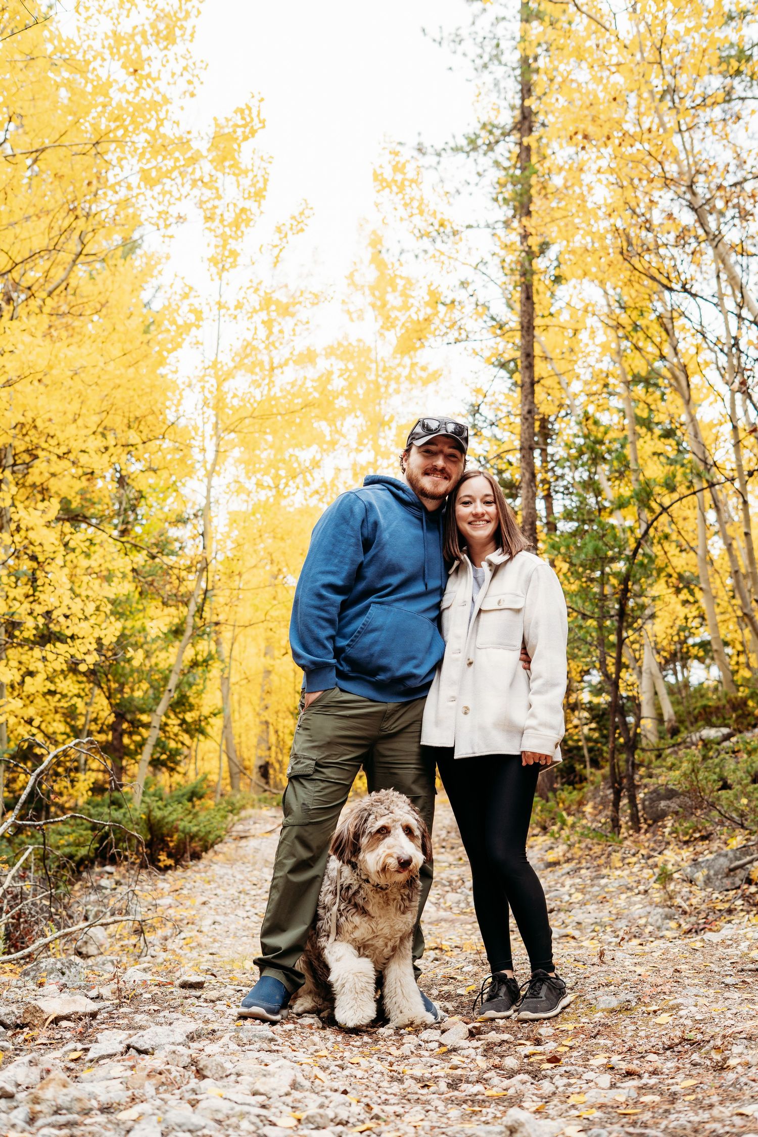 Outdoor couples photography session in Clear Creek, Colorado featuring a couple smiling at the camera with their dog among yellow fall leave