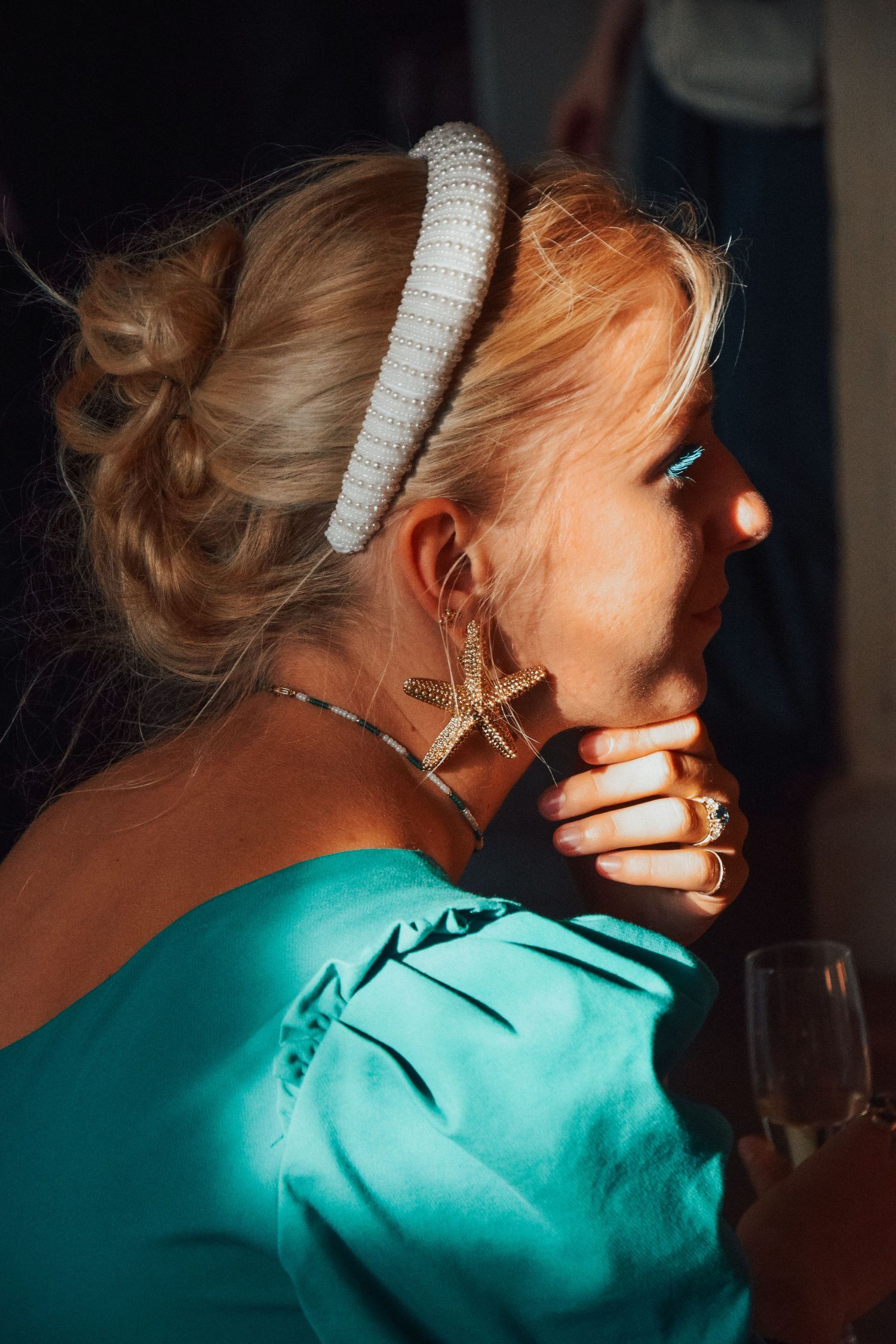 Profile view of someone wearing a pearl headband and turquoise dress at a formal event.