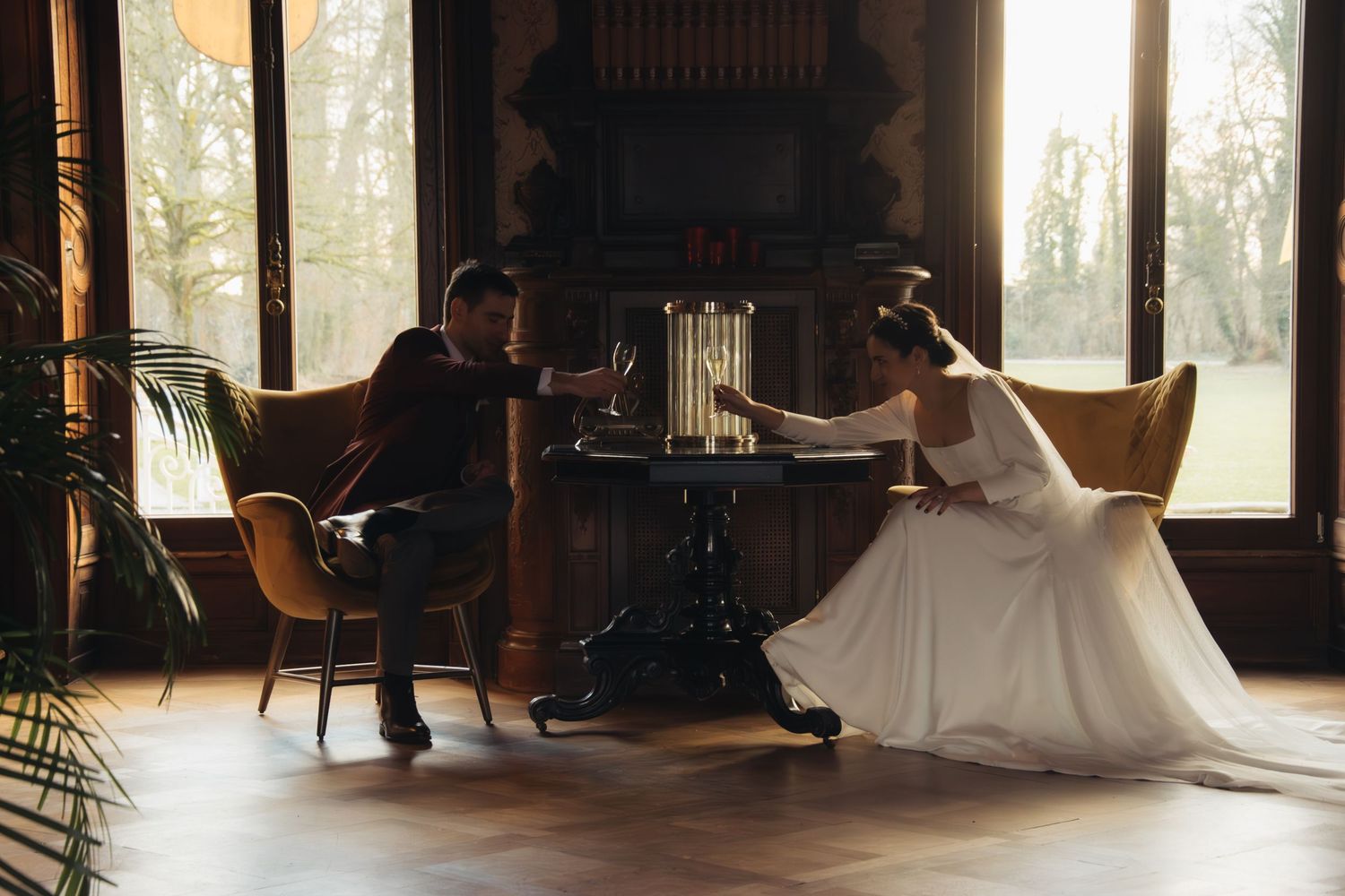 A wedding couple poses playfully at a vintage piano in a sunlit room.