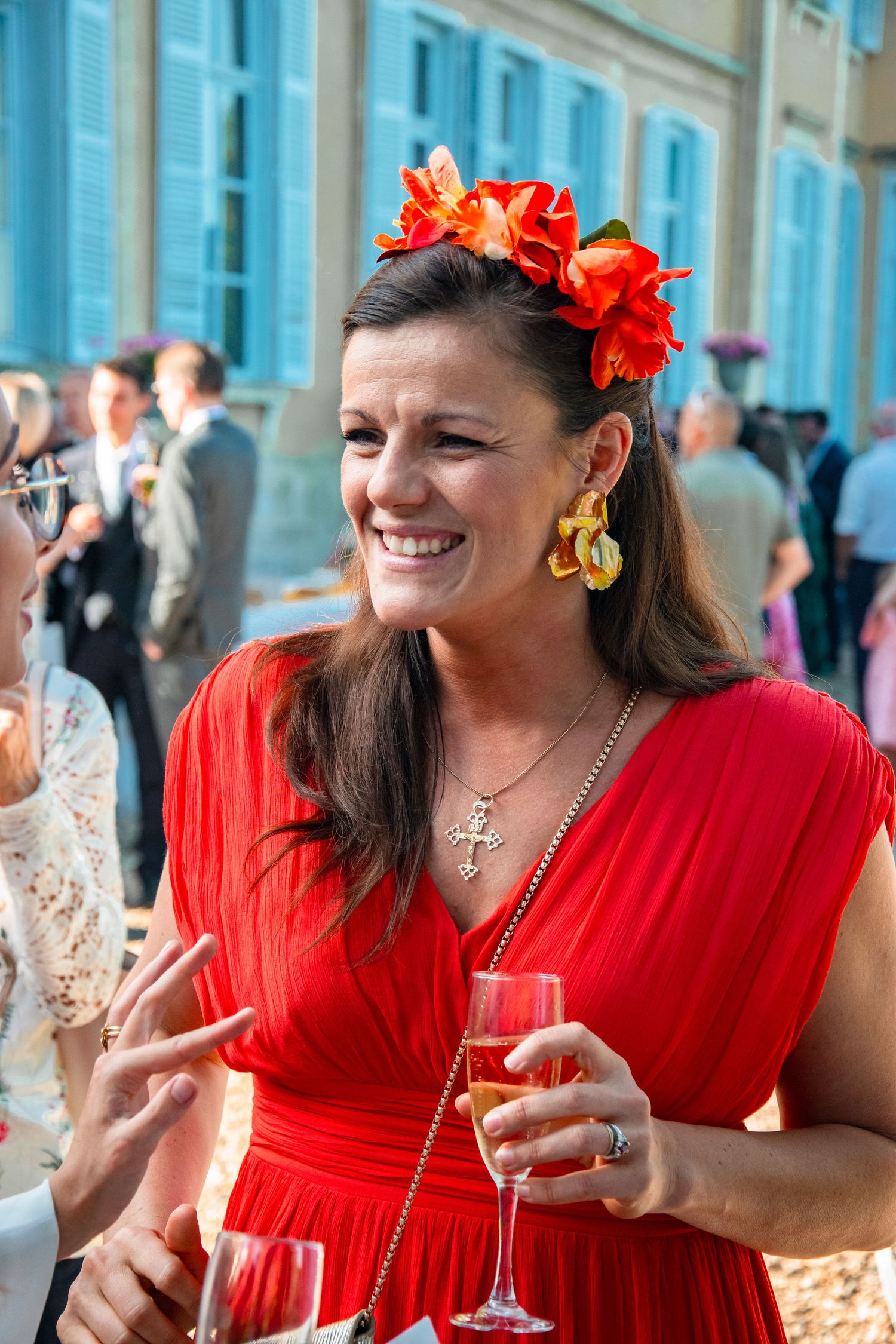 A guest in a red dress and floral crown enjoying a celebratory drink outdoors.