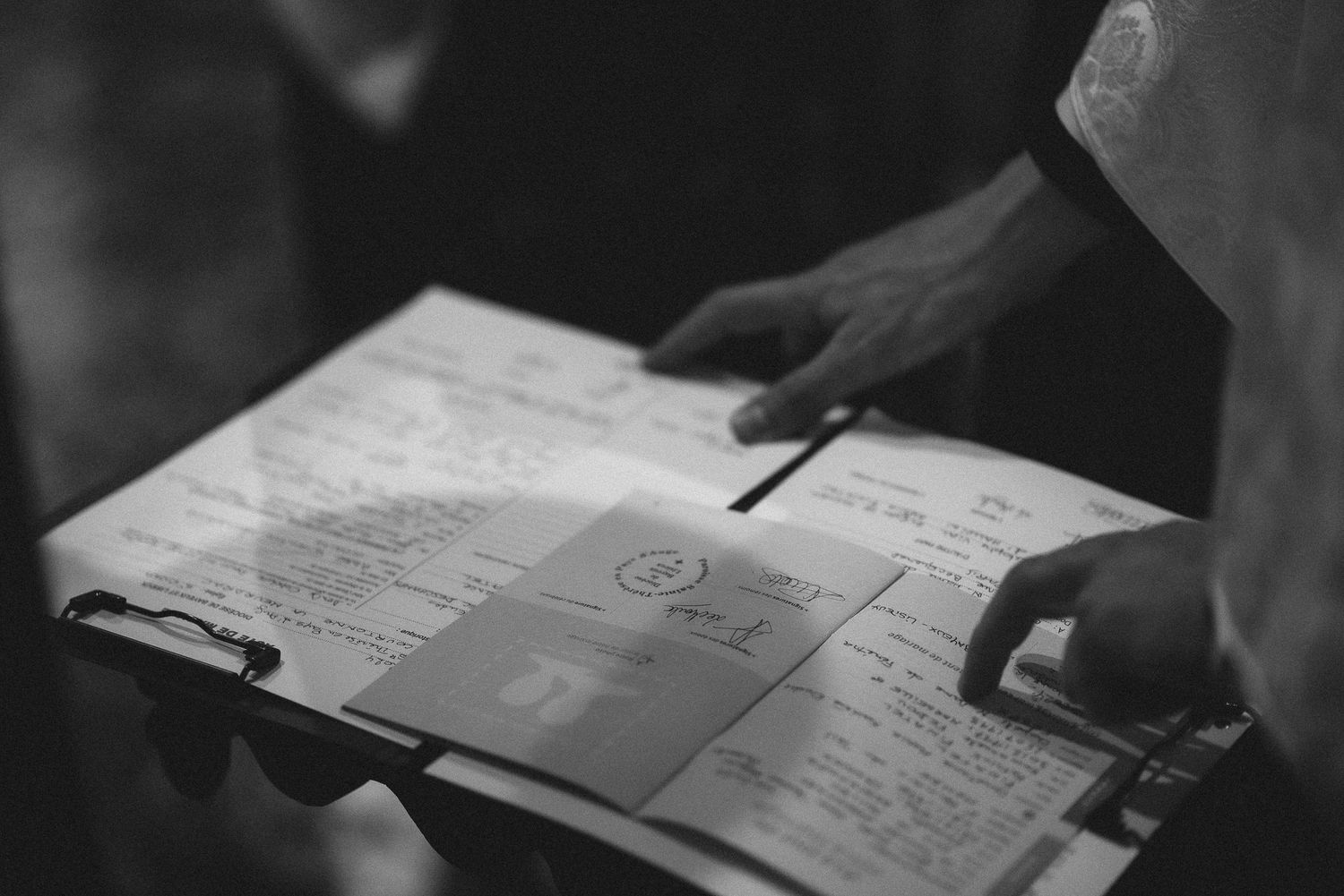 Black and white image of hands signing marriage certificate or registry document.
