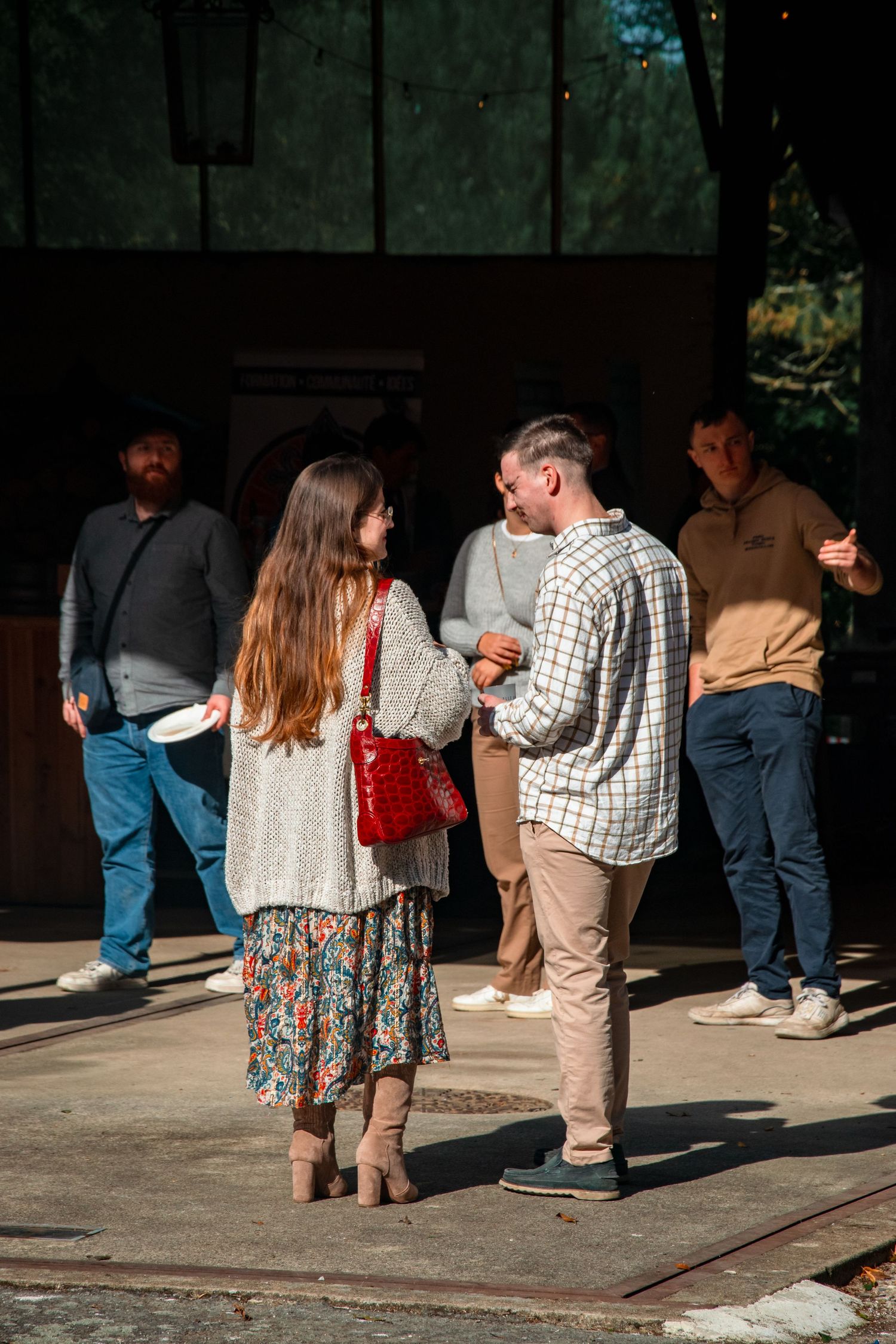 People gathered in casual conversation outside a building on a sunny day.