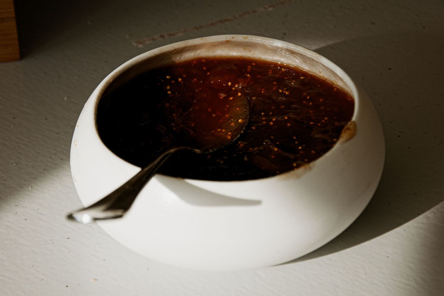 Stirring a spoon in a dark bowl of liquid on a dimly lit table with dramatic shadows.