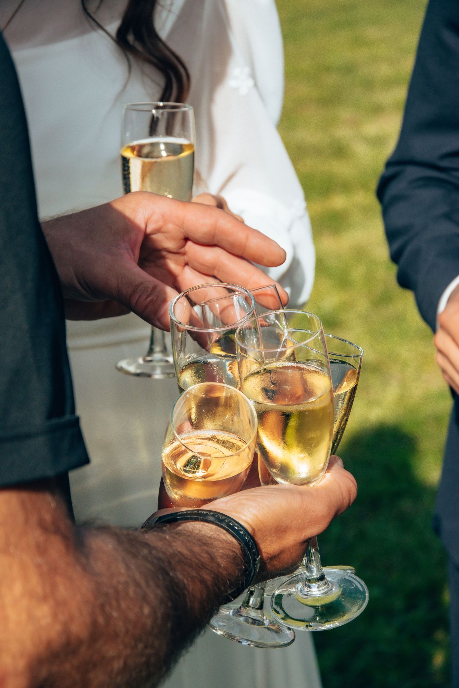 Hands holding champagne glasses for a celebratory toast at an outdoor wedding.