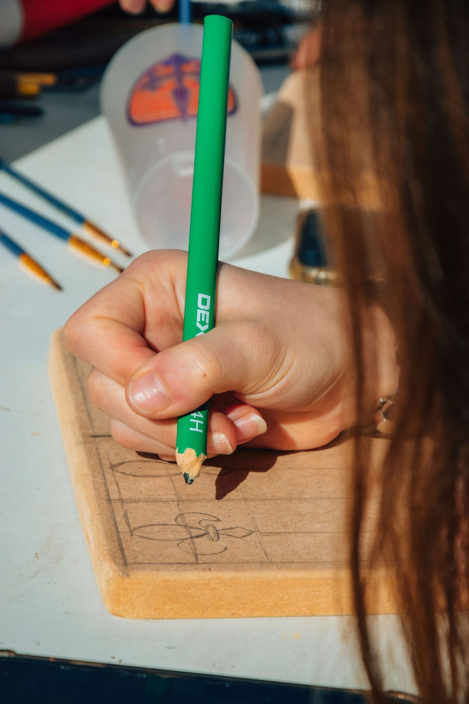 Close-up of hands holding a green pencil while drawing on a wooden surface.