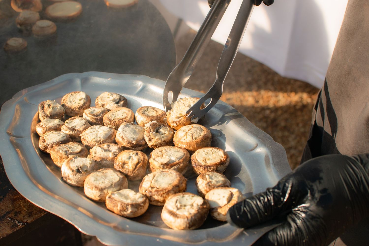 Platter of grilled mushrooms being served with tongs at a catered event.
