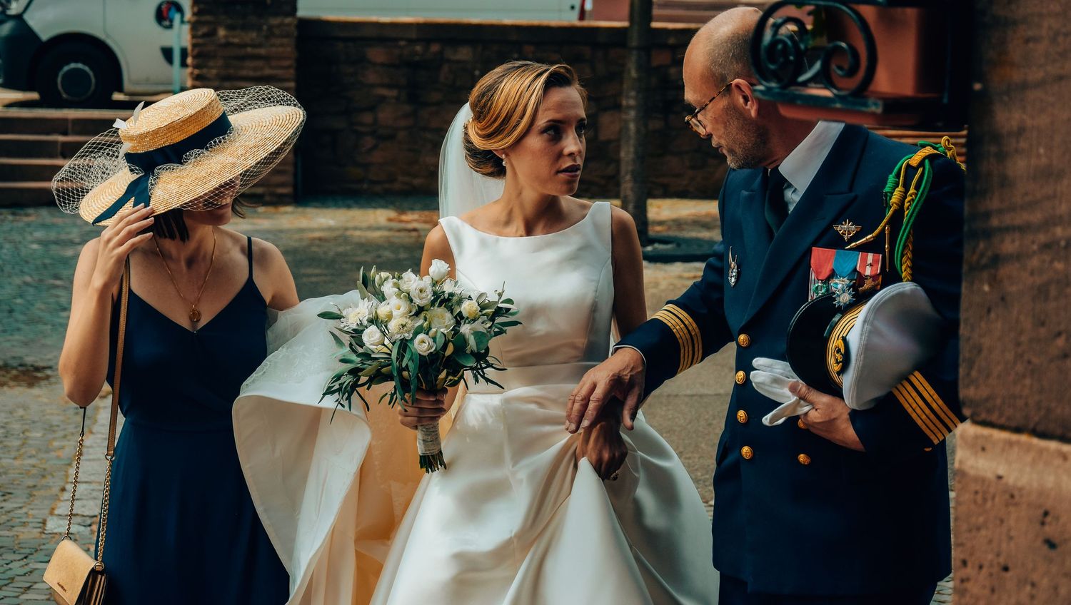 Bride in classic white dress holding bouquet while walking with guests.