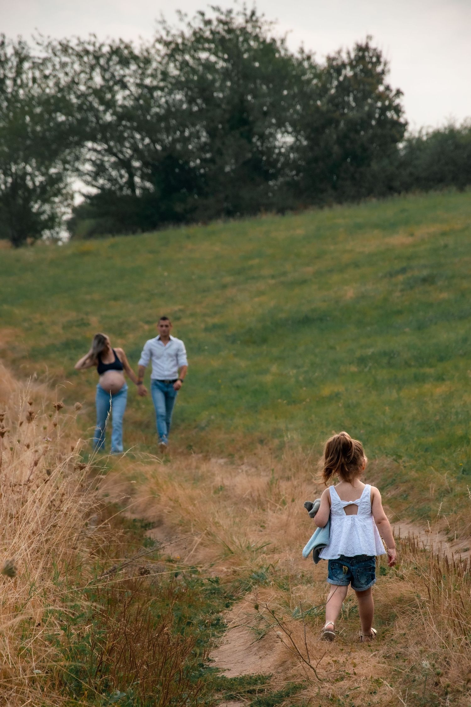 People walking along a winding dirt trail through a grassy hillside.