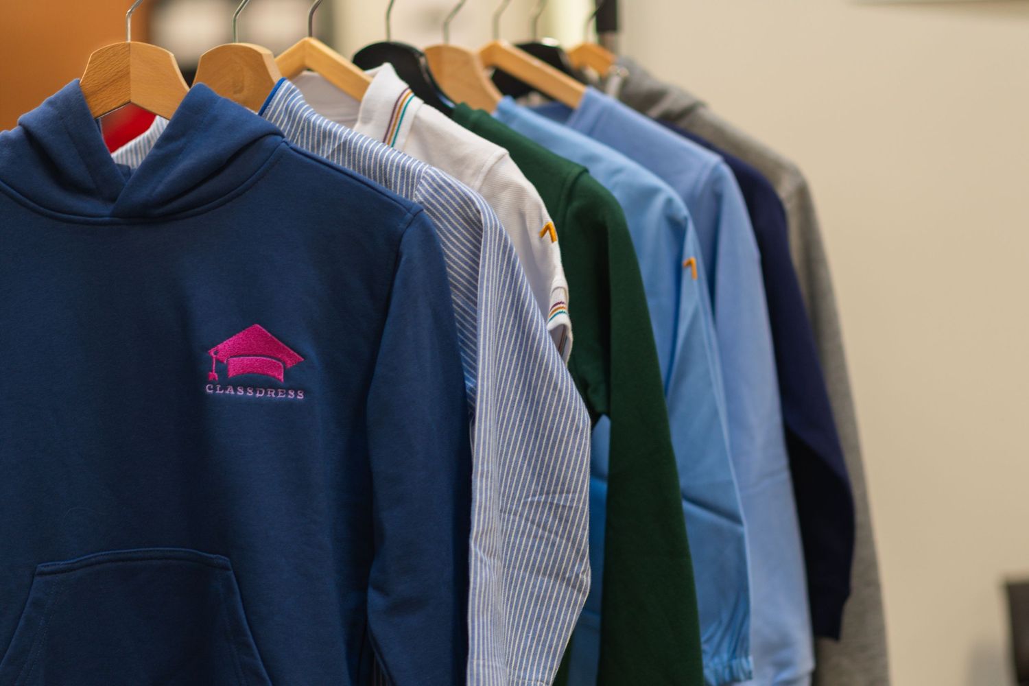 Row of collegiate hoodies and shirts hanging on clothing rack in navy and light blue colors.