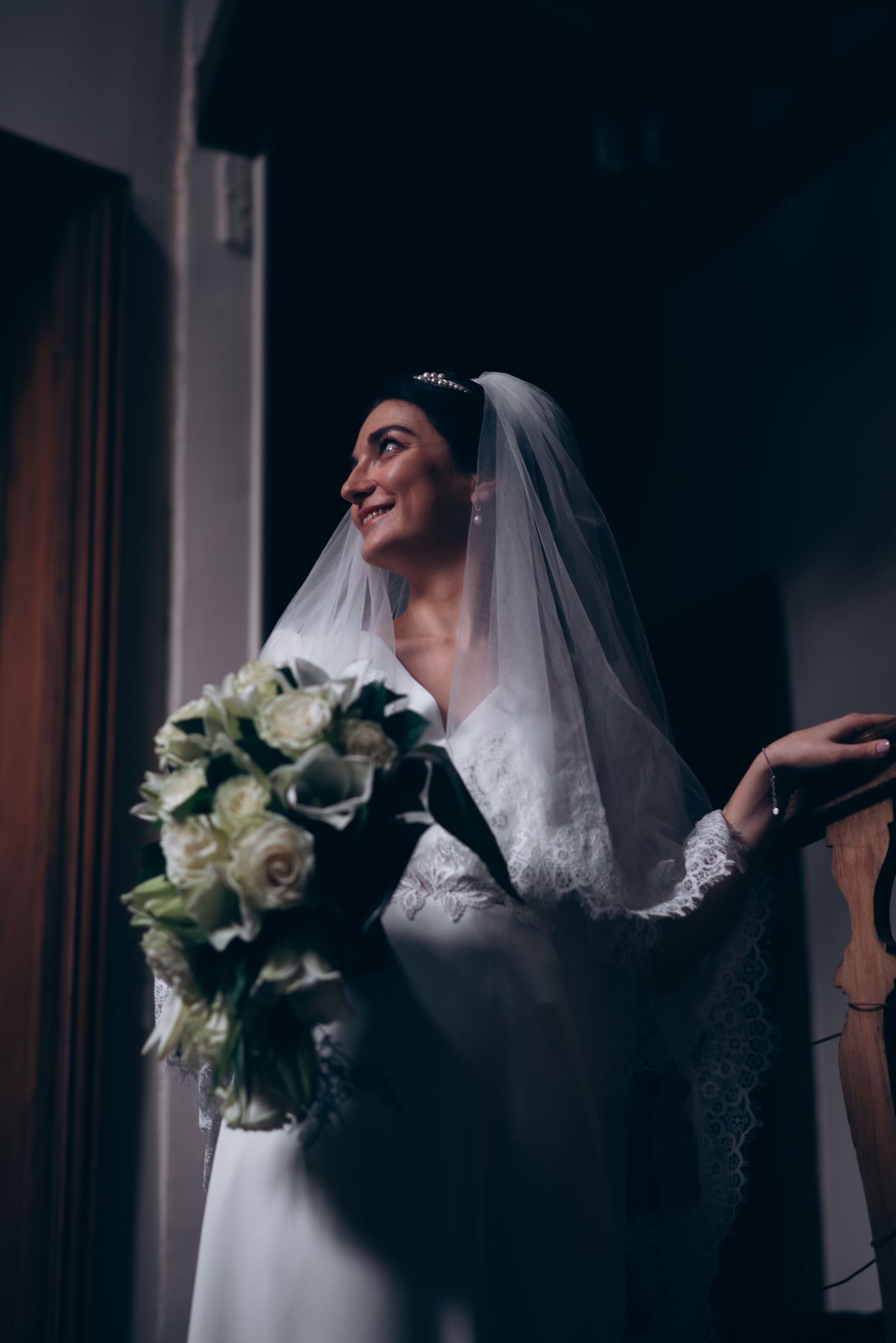 Bride in white lace dress holding bouquet of white roses.