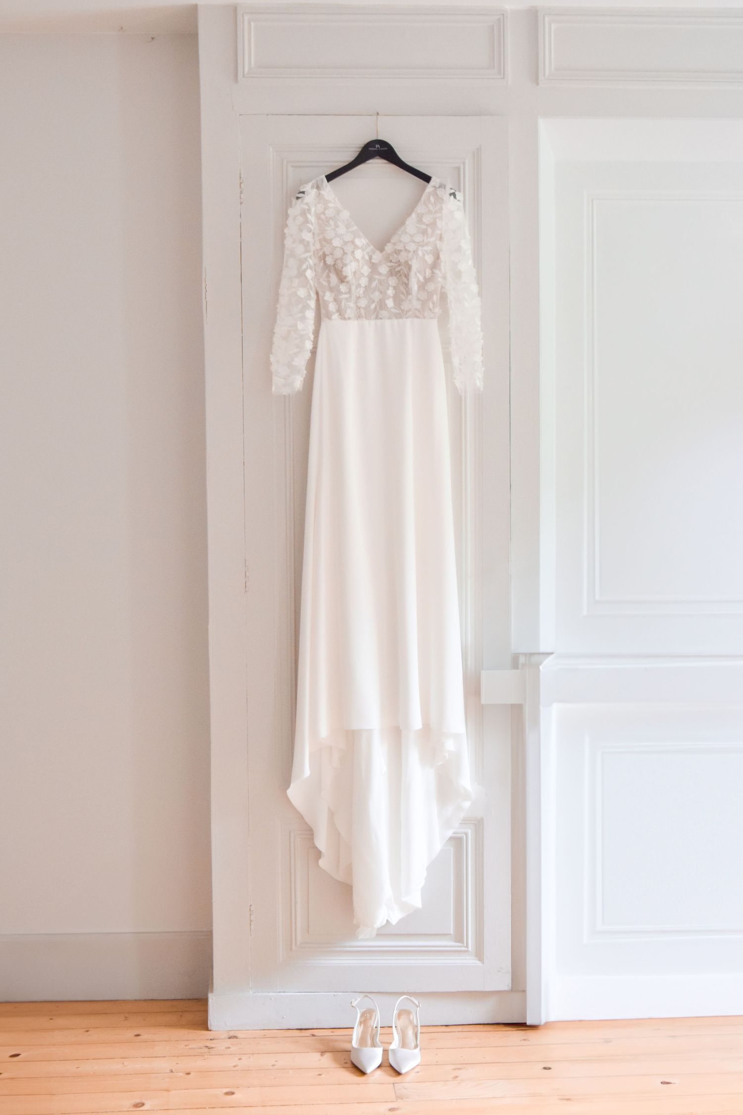 Elegant white wedding dress with lace sleeves hanging on door with shoes beneath.