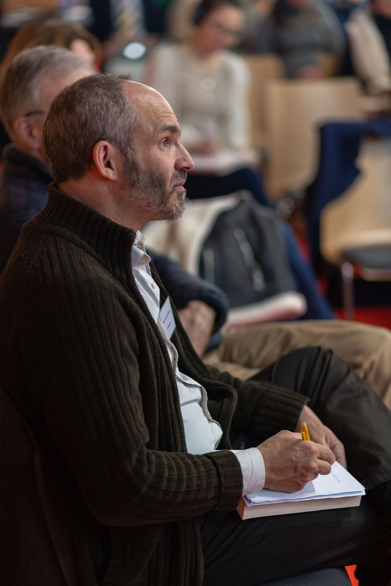 Side profile of someone writing notes in a darkly lit classroom setting while wearing a brown sweater.
